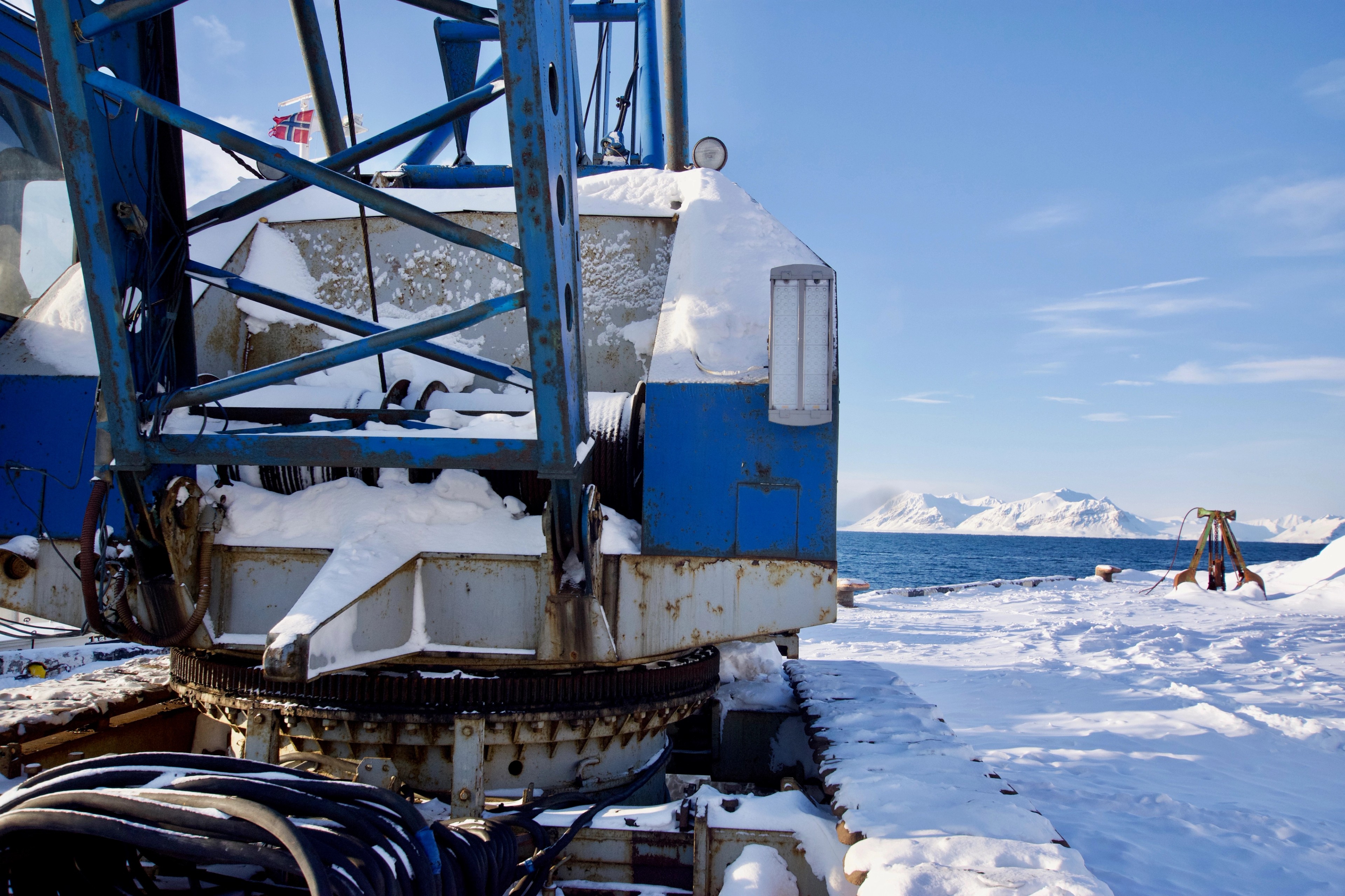 A blue industrial structure rises from the snow beside the coast.