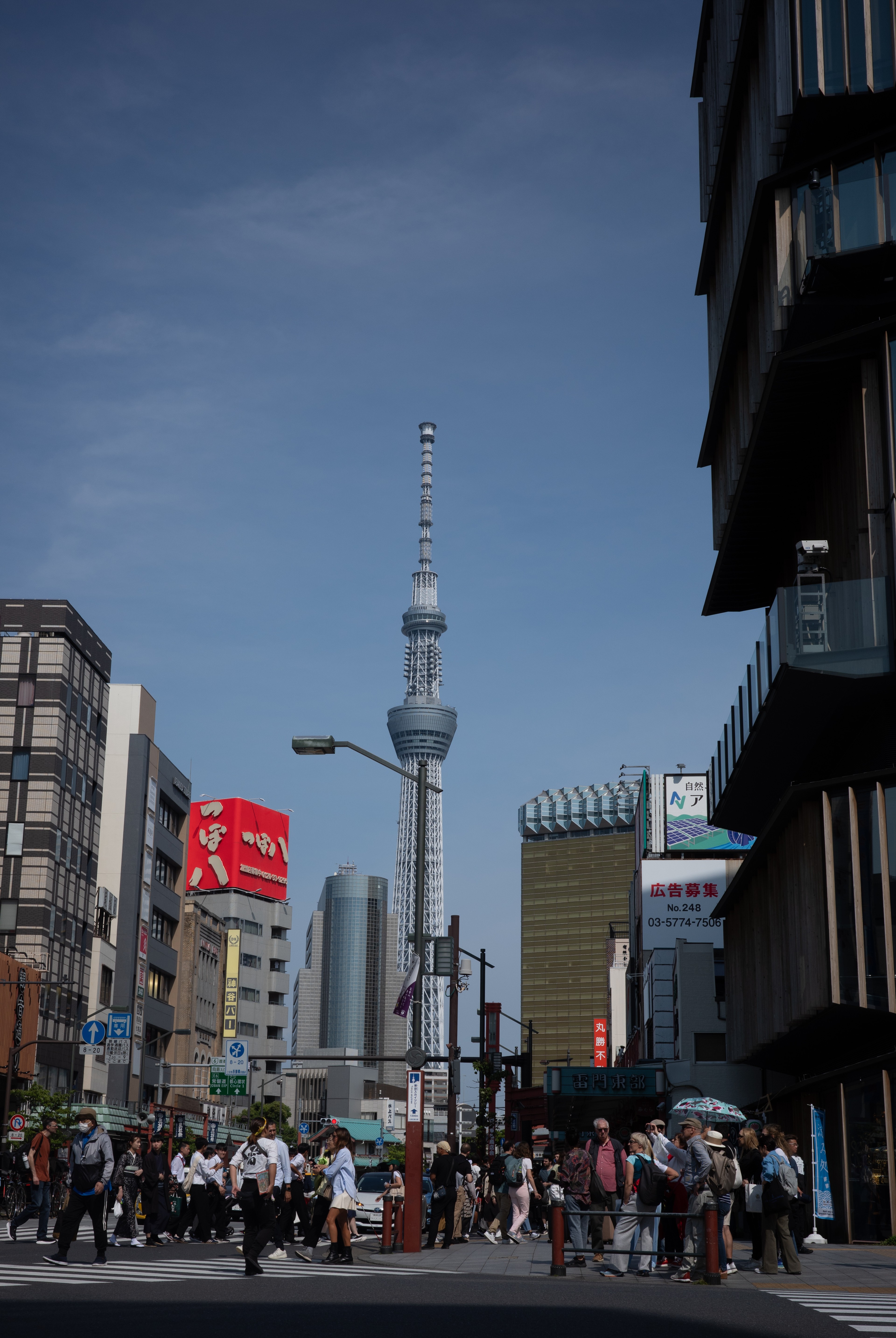 A busy city crossing with the Tokyo Skytree rising between buildings.