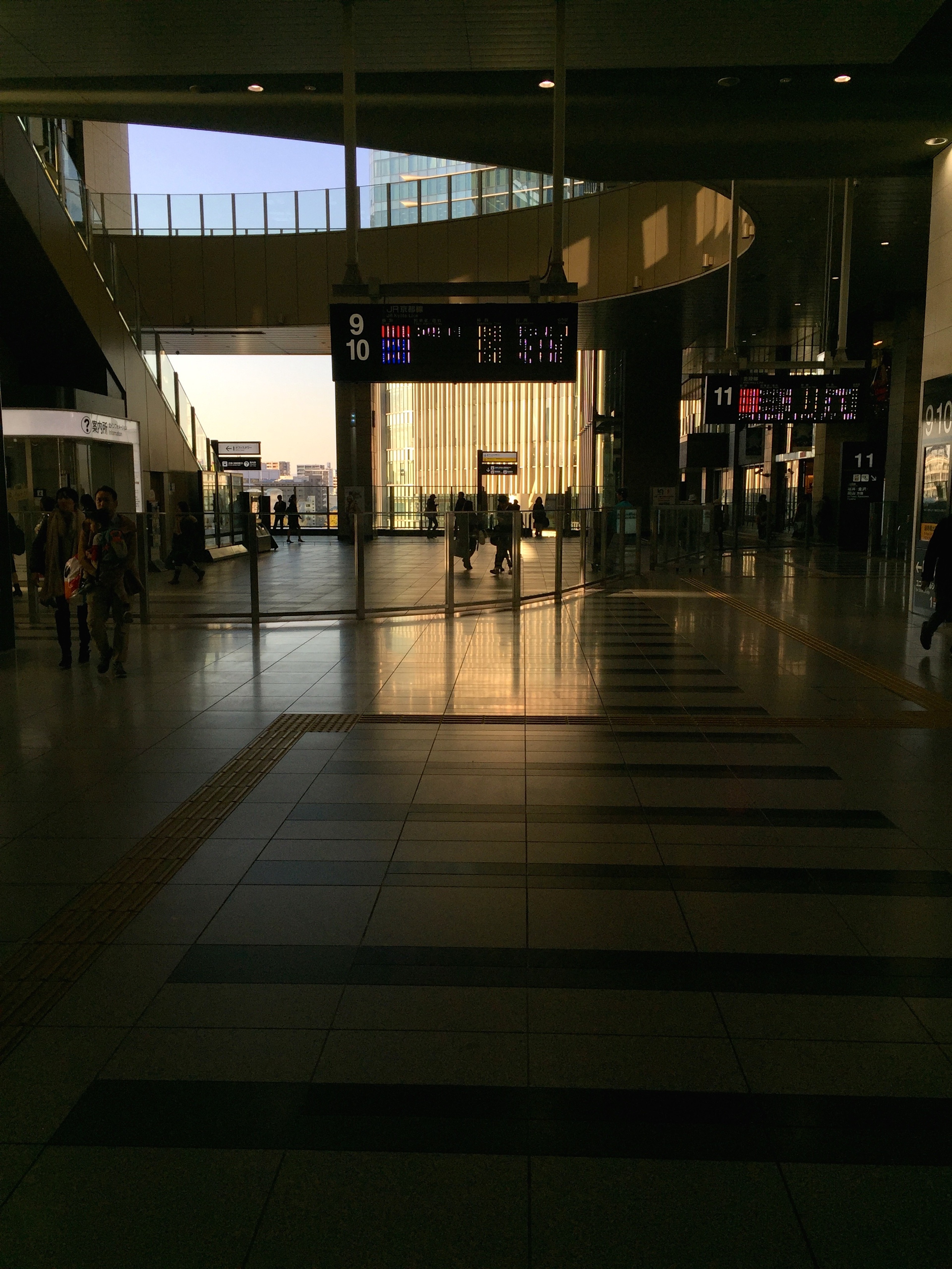 A quiet indoor corridor opens toward a brightly lit shopping area.