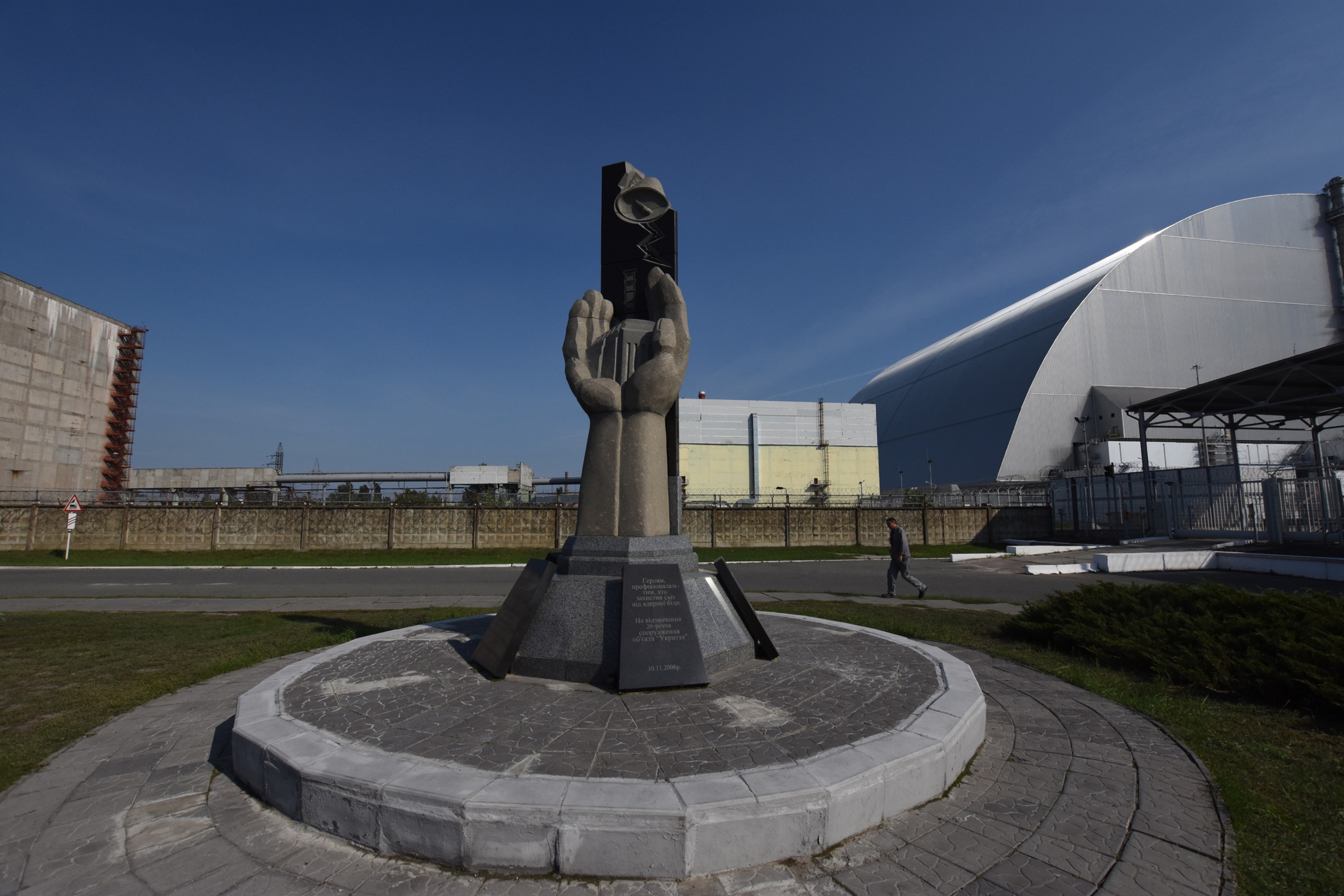 A memorial monument stands before the New Safe Confinement structure.