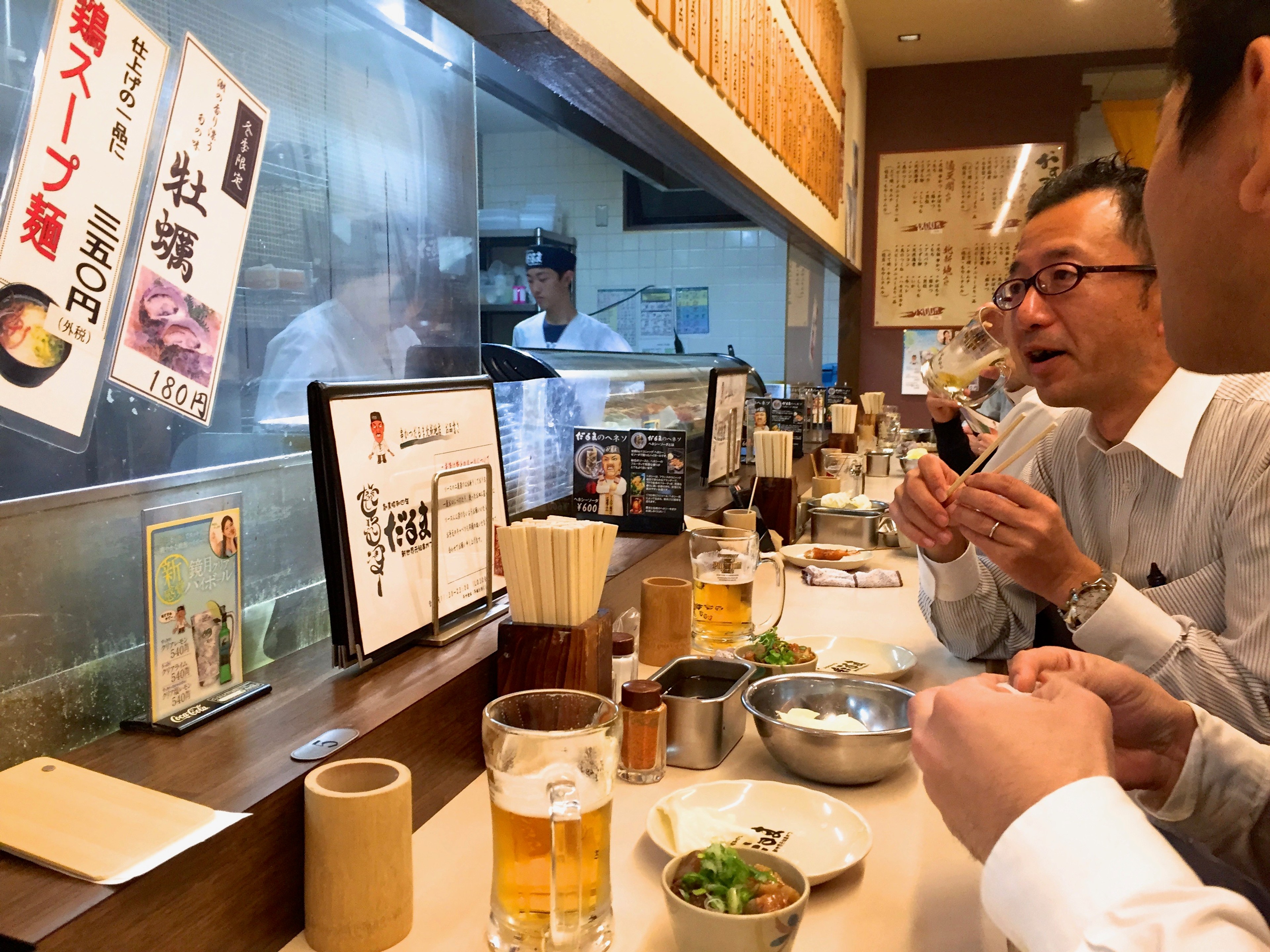 Diners sit at a restaurant counter beneath menu signs.