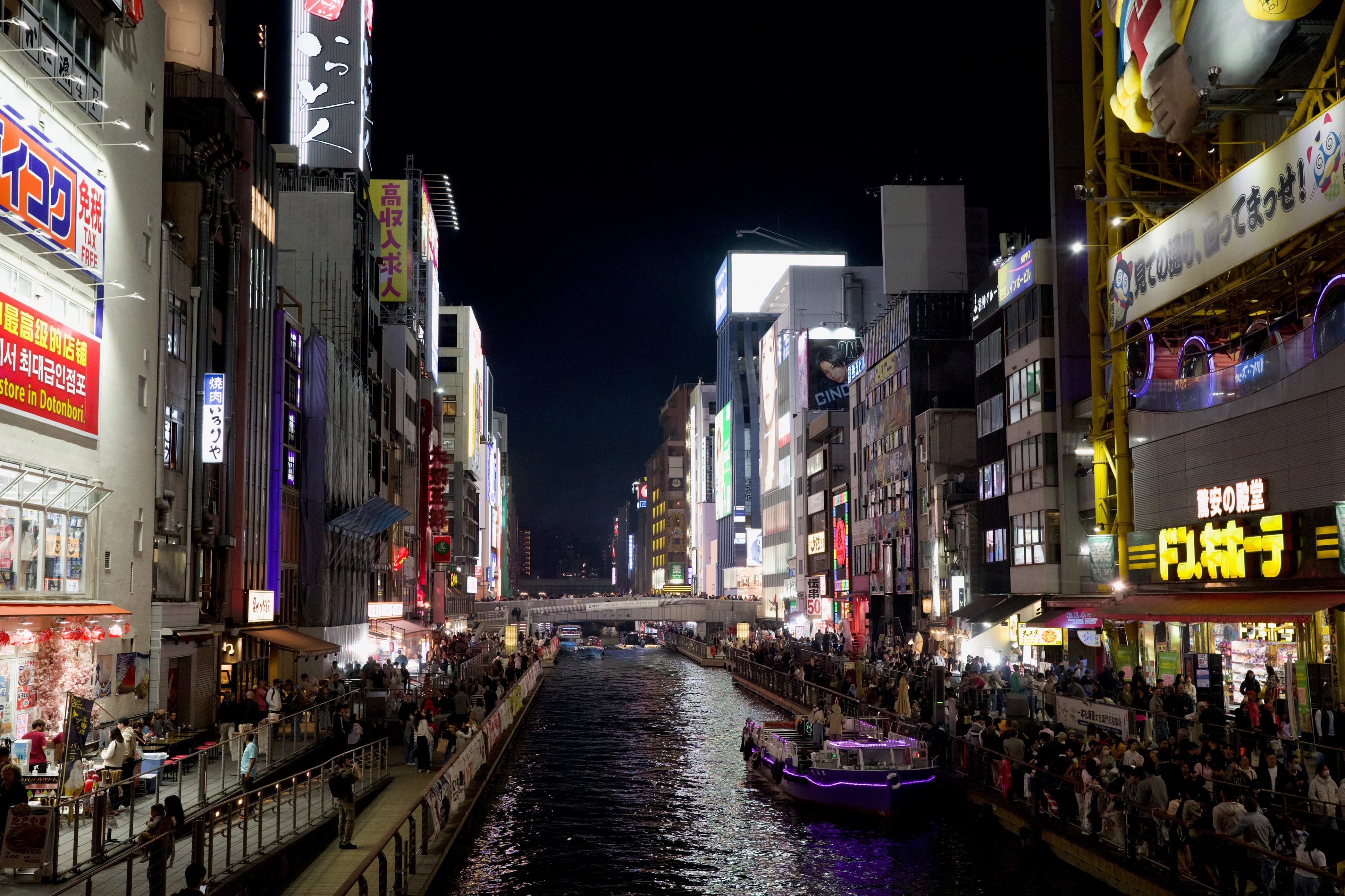 Neon signs and crowds line a city street at night.