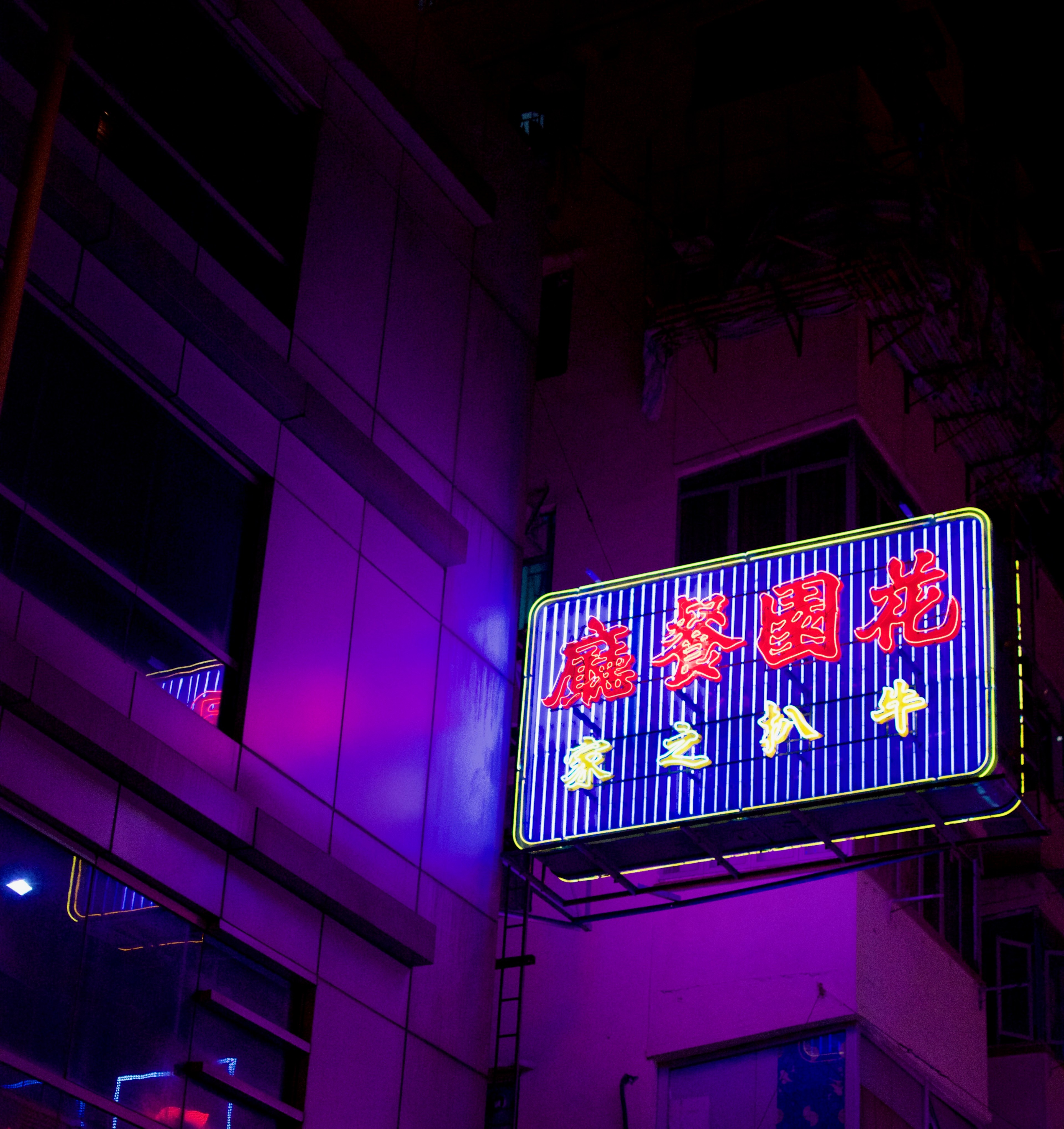 A blue neon sign with red Chinese characters lights a building corner at night.