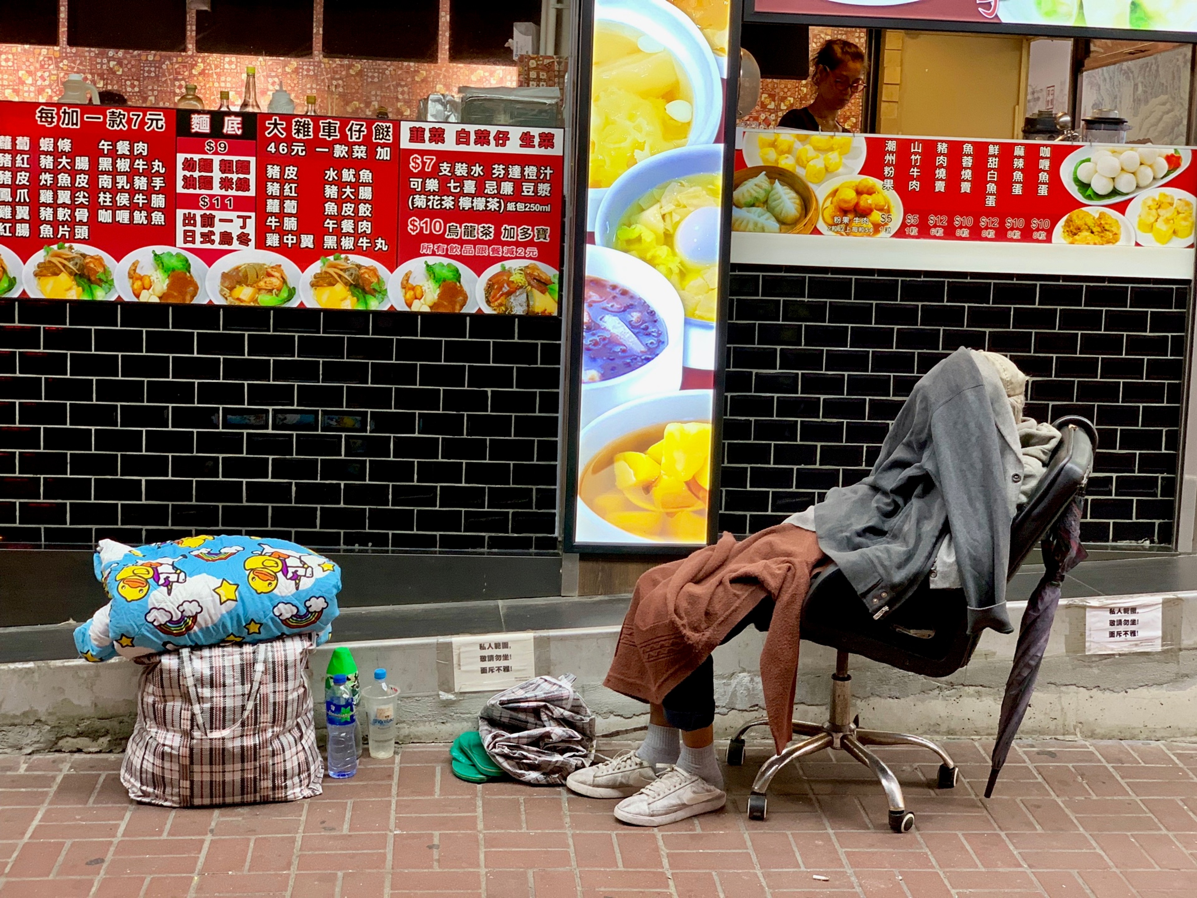 Street food stall beside a Hong Kong road, with a seated person and menu.