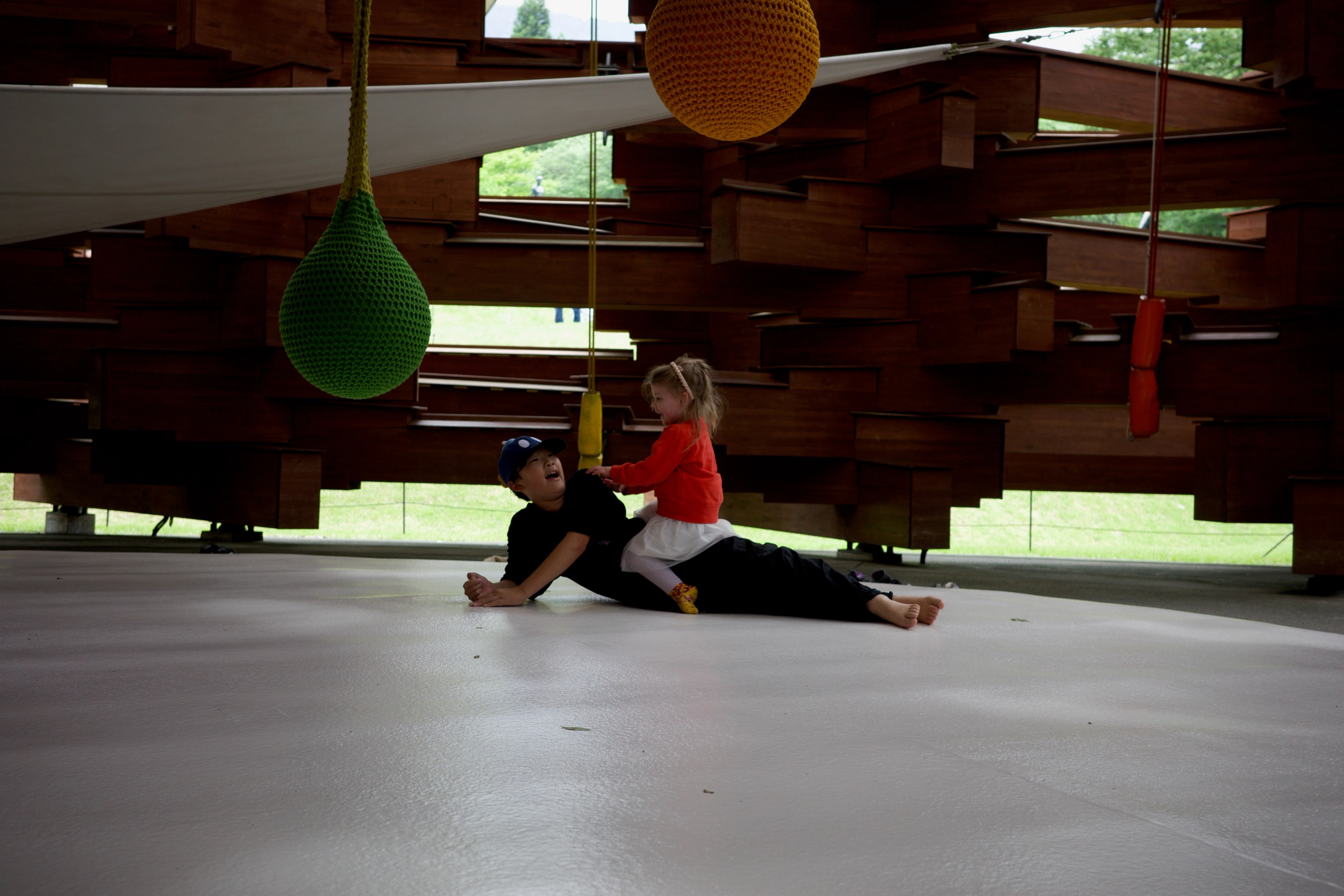 A toddler crawls beneath colorful hanging shapes inside a timber structure.