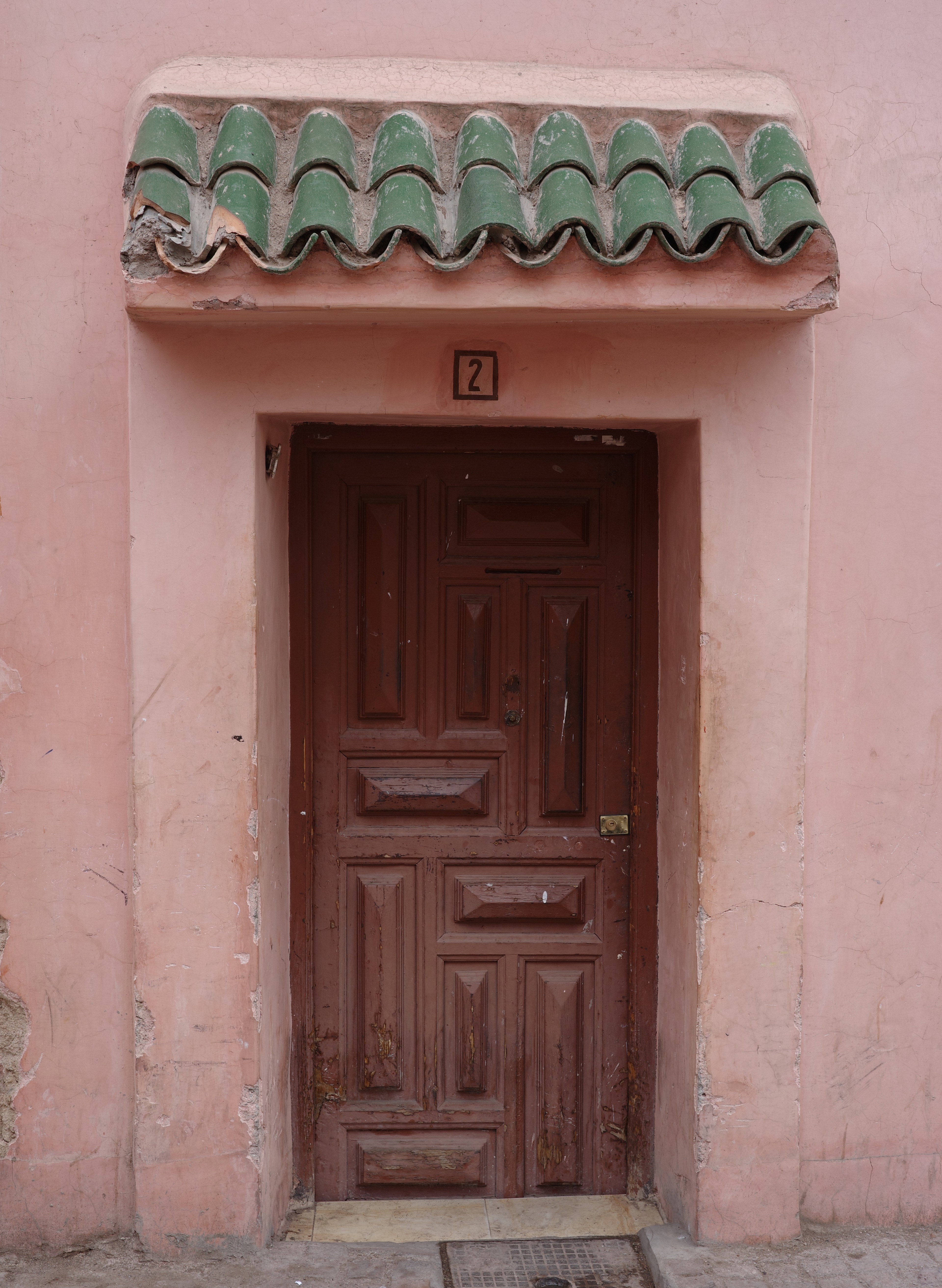 A carved wooden door sits beneath a small green-tiled awning in a pink wall.