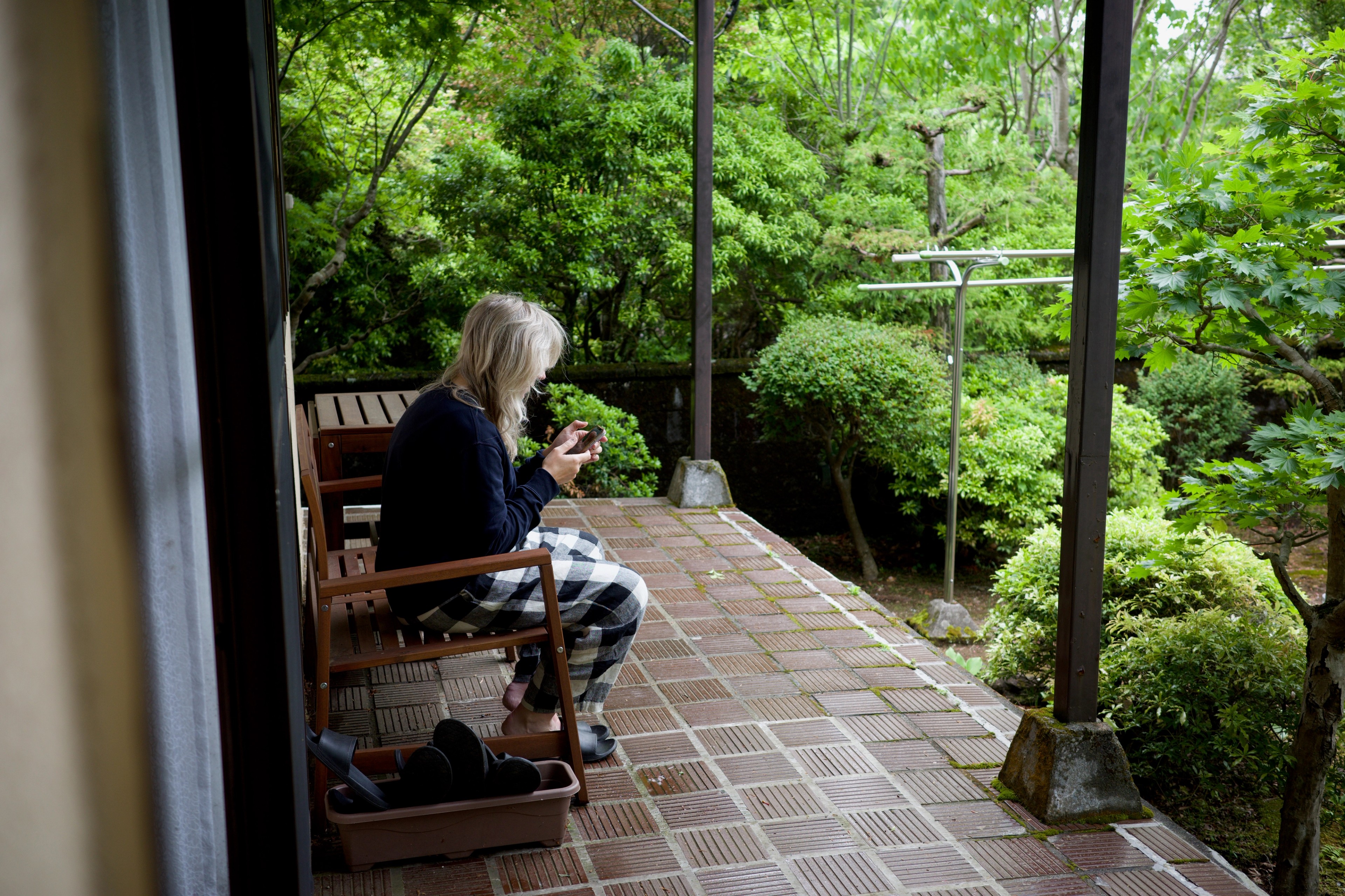 A person sits on a veranda overlooking a lush garden.