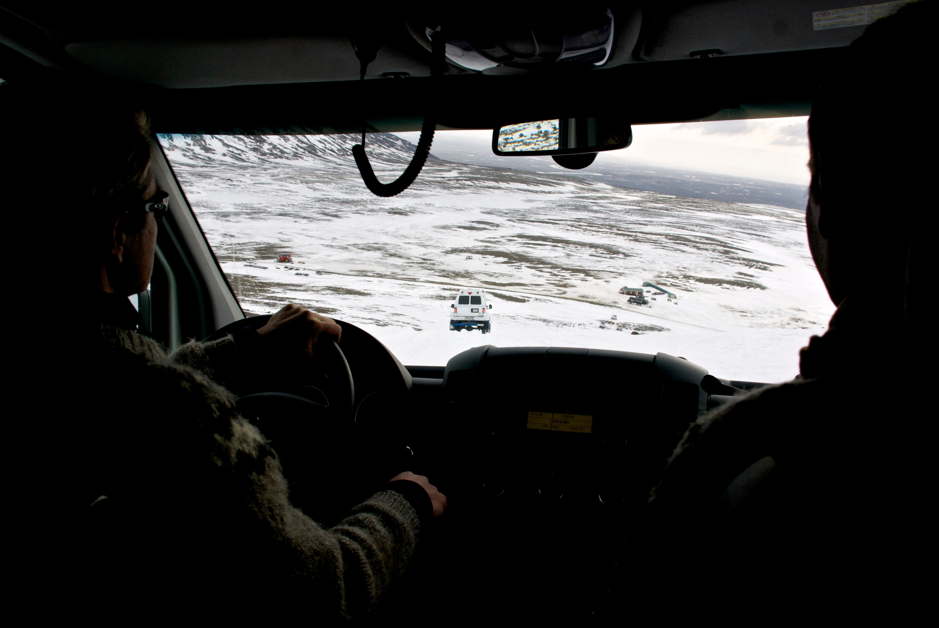 A driver looks through a vehicle windshield across a snowy landscape.