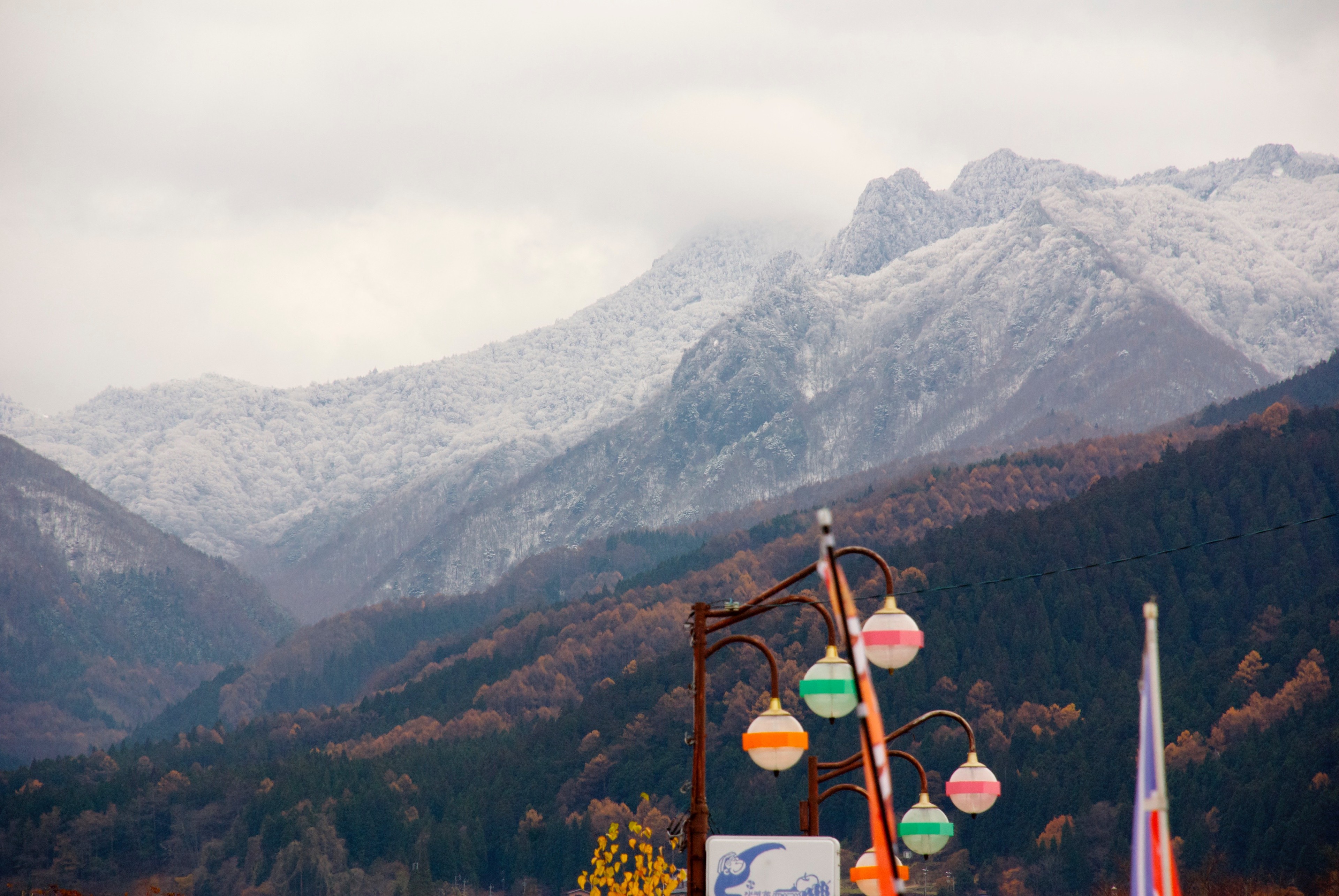 A snowy mountain rises above a roadside view with signs and flags.