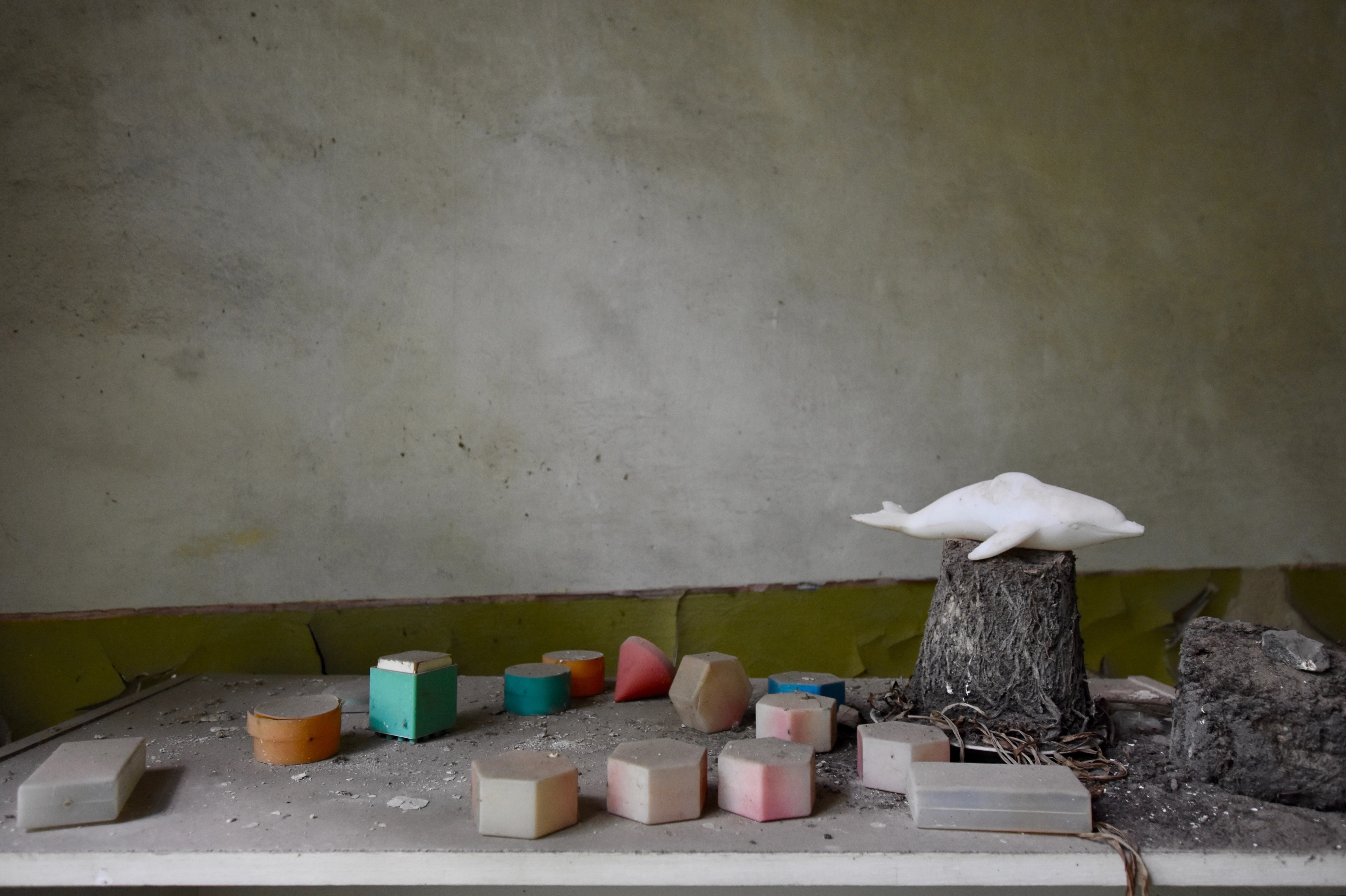 Small containers and objects line a low shelf in a damaged room.