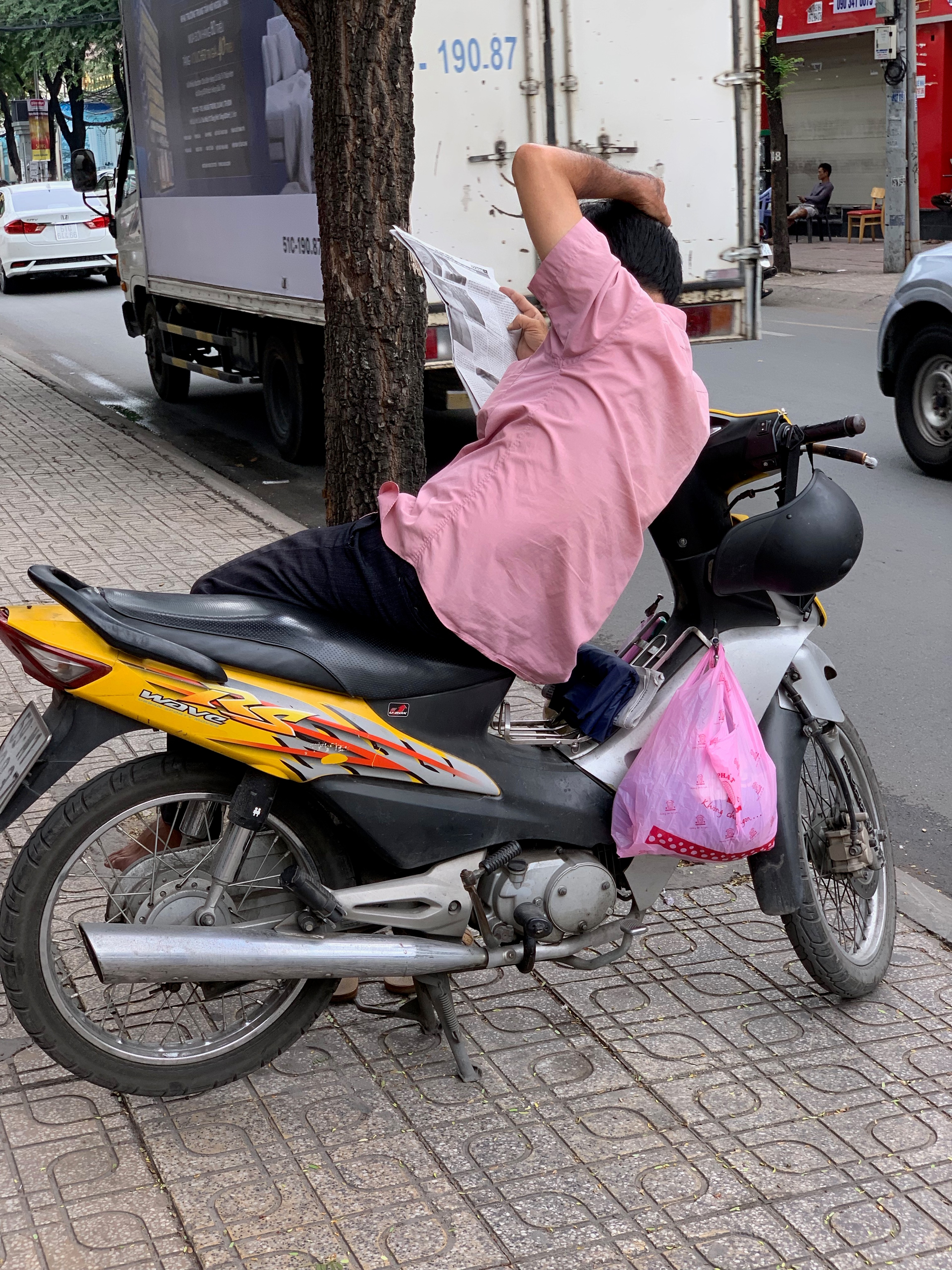 A woman in pink rides a yellow scooter along the street.