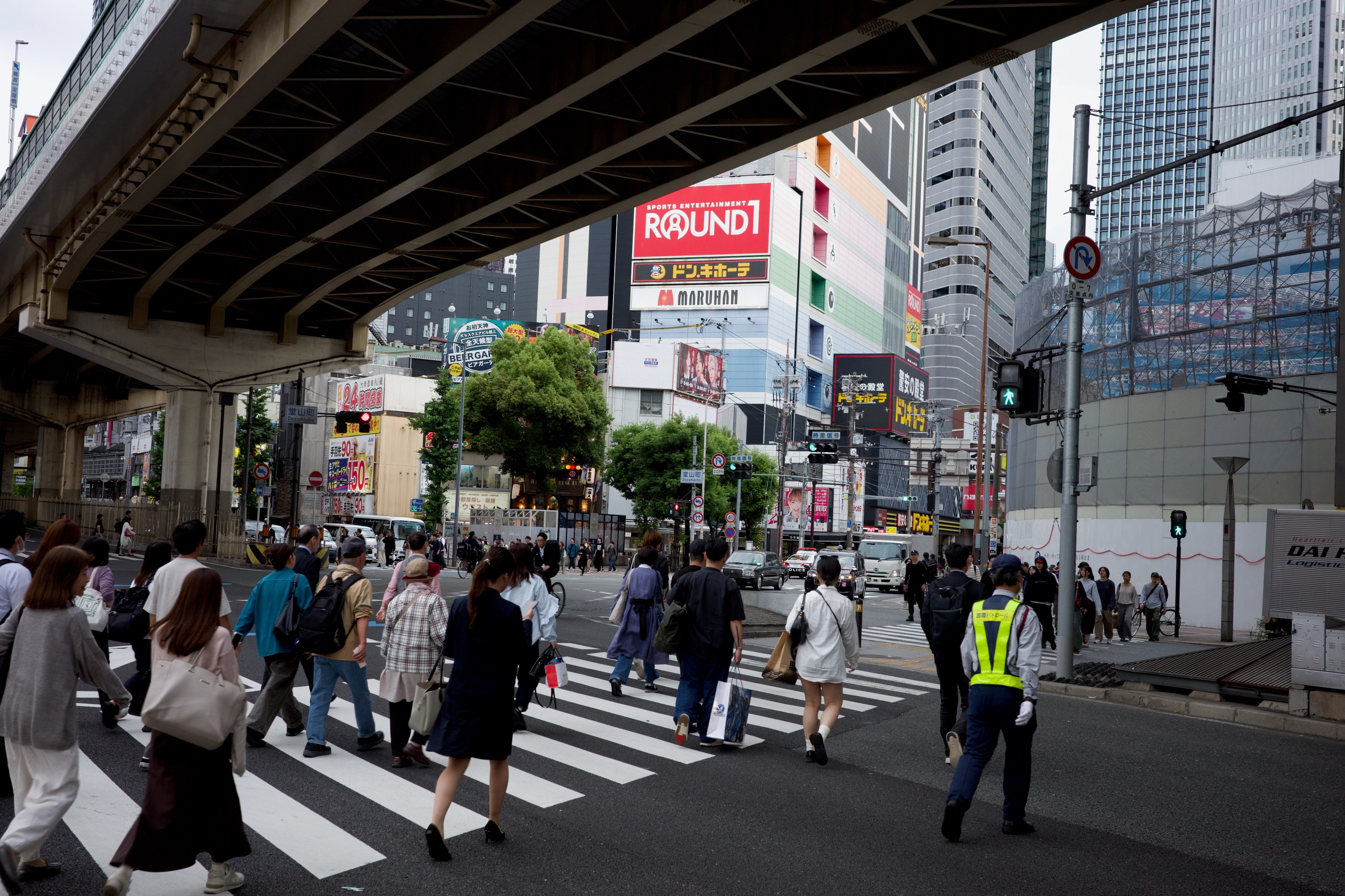 Pedestrians cross a city street beneath an elevated roadway.