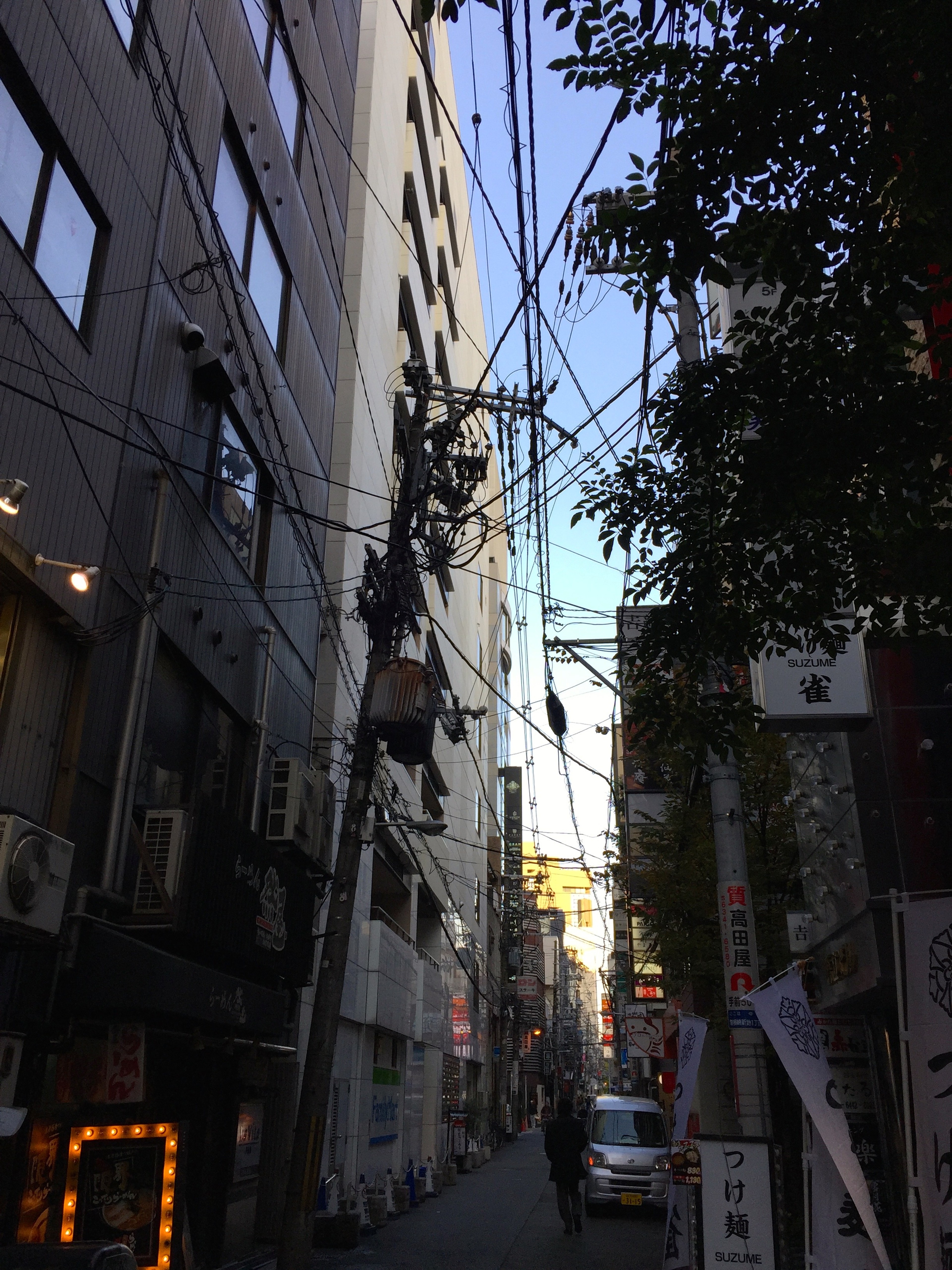 A narrow city alley runs between tall buildings and overhead utility wires.