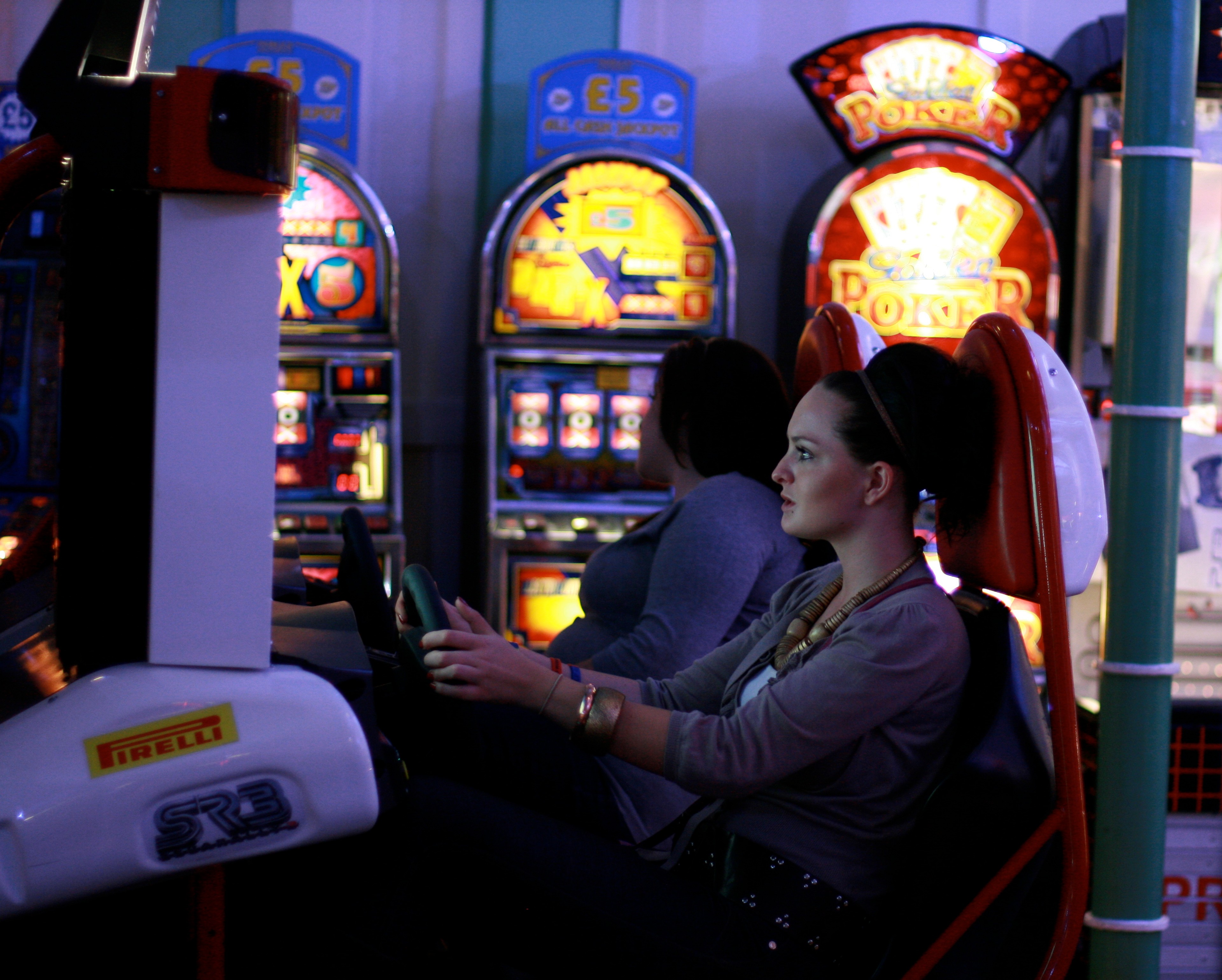 A woman plays an arcade game beneath illuminated machines.