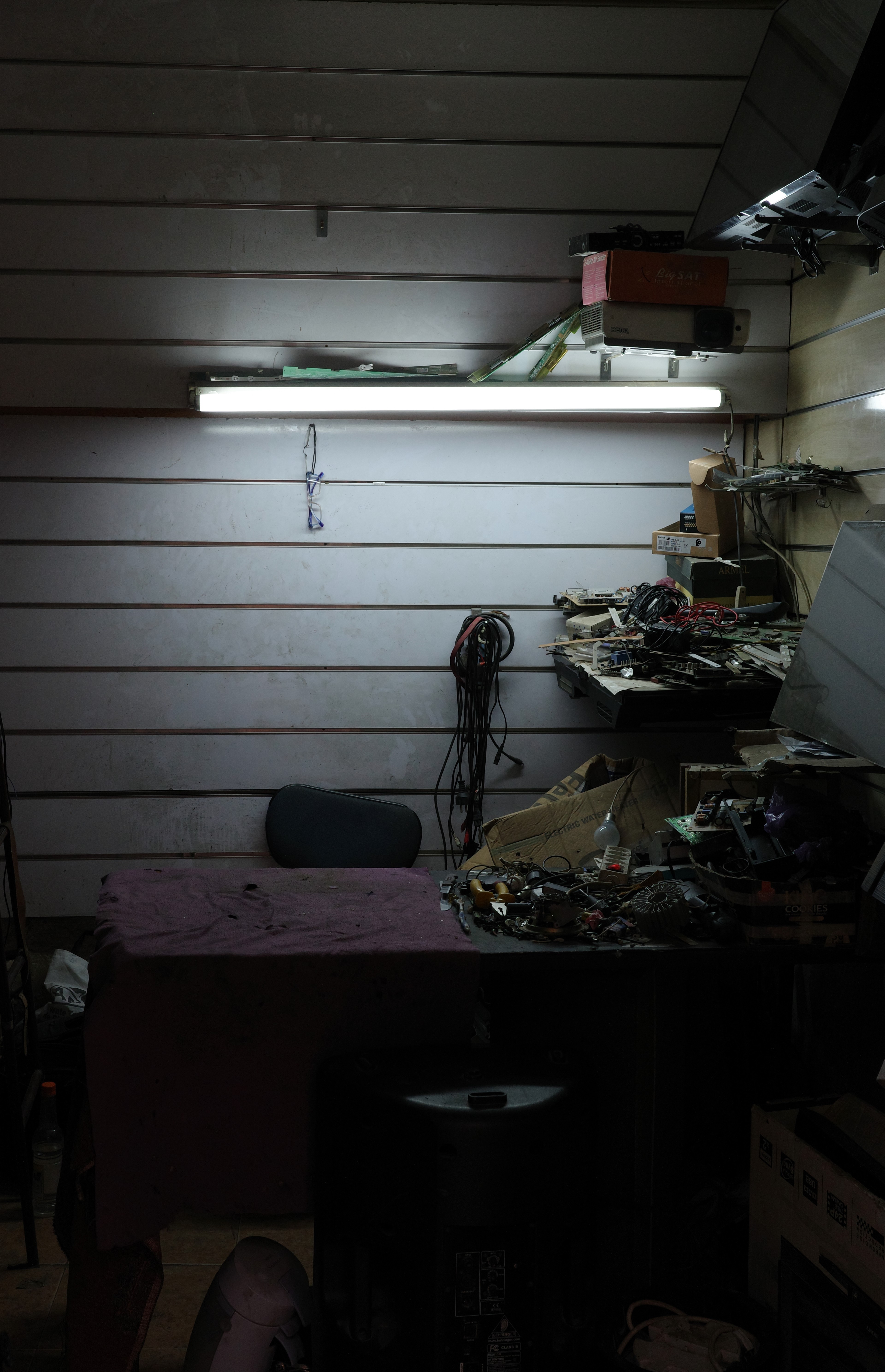 A worker sits at a machine in a small, fluorescent-lit workshop.