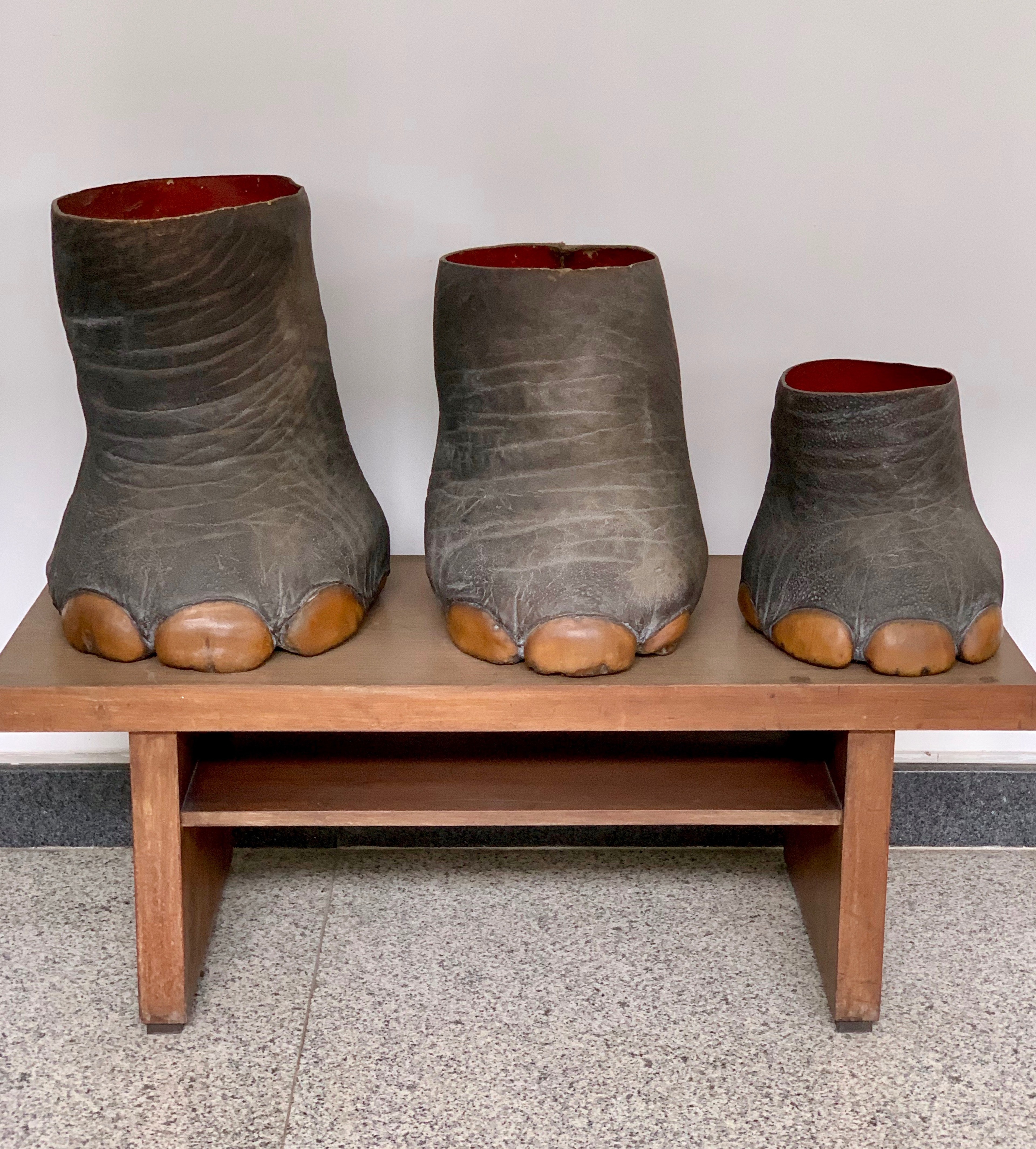 Three carved stone boots sit on a low wooden stand in a gallery.