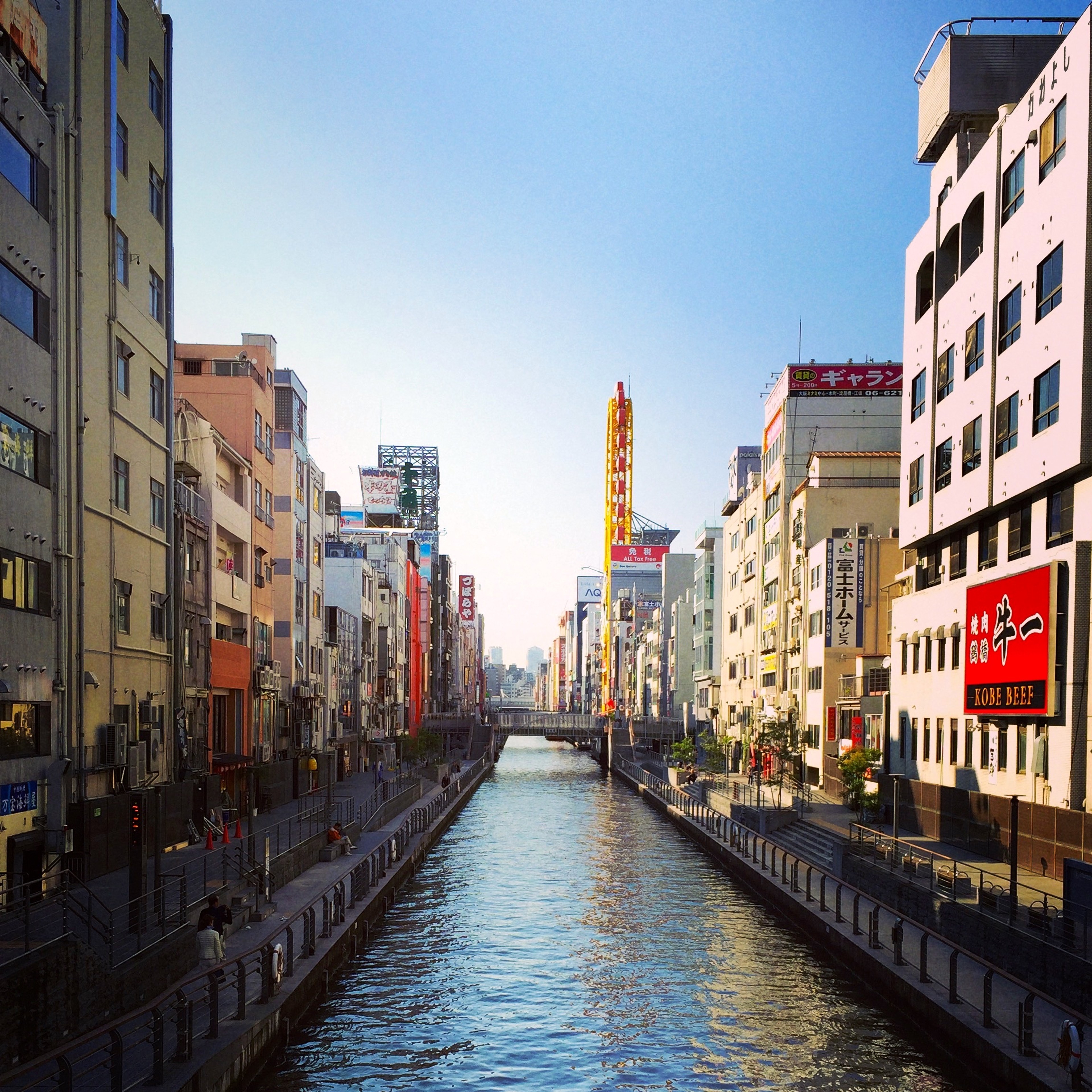 A canal passes between tall buildings and a row of waterside restaurants.