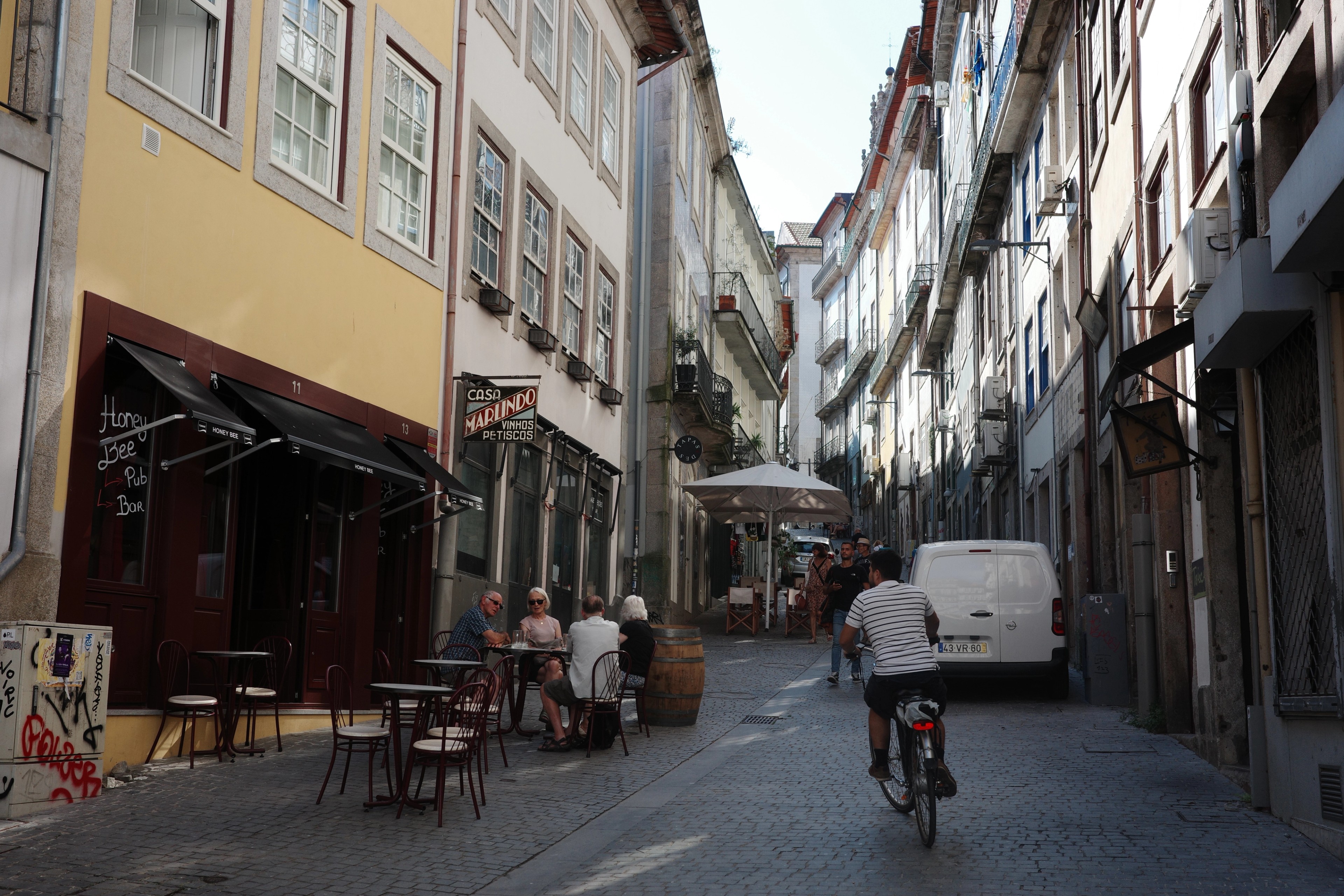 A cyclist rides down a narrow Porto street lined with tall buildings and café tables.