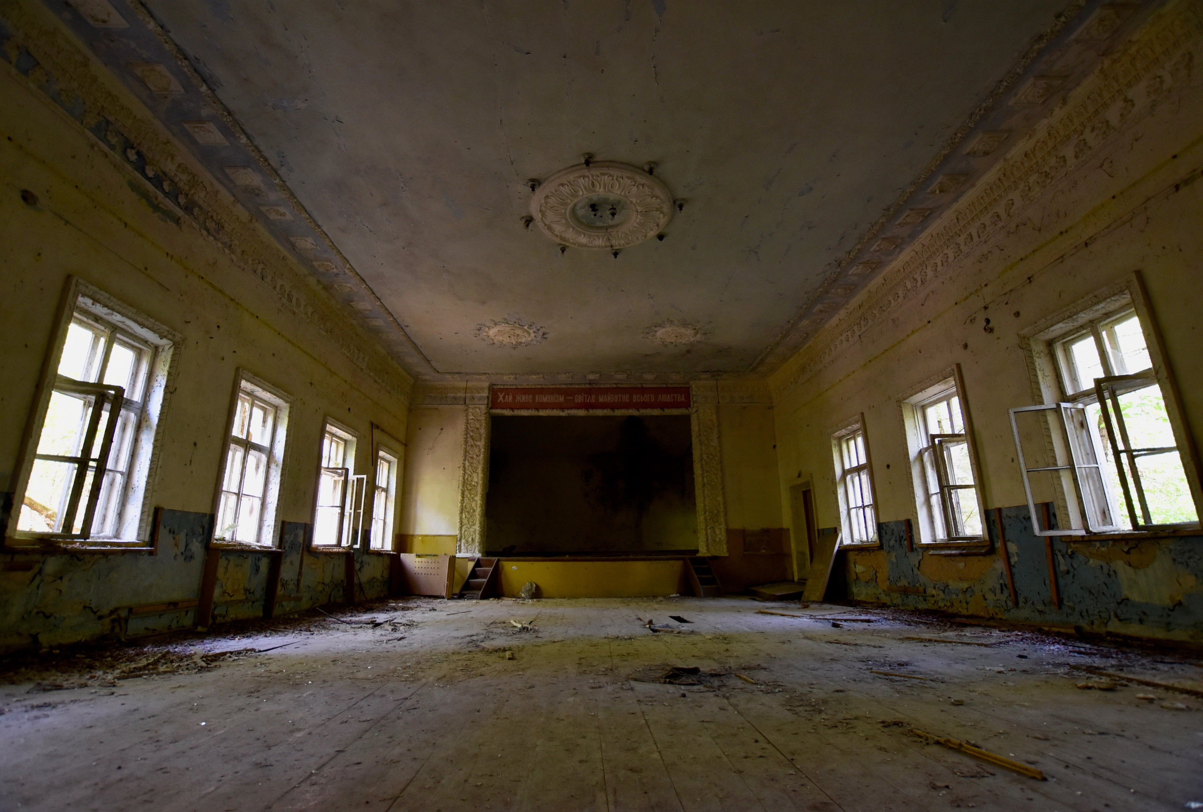 An empty room with tall windows and a damaged ceiling.