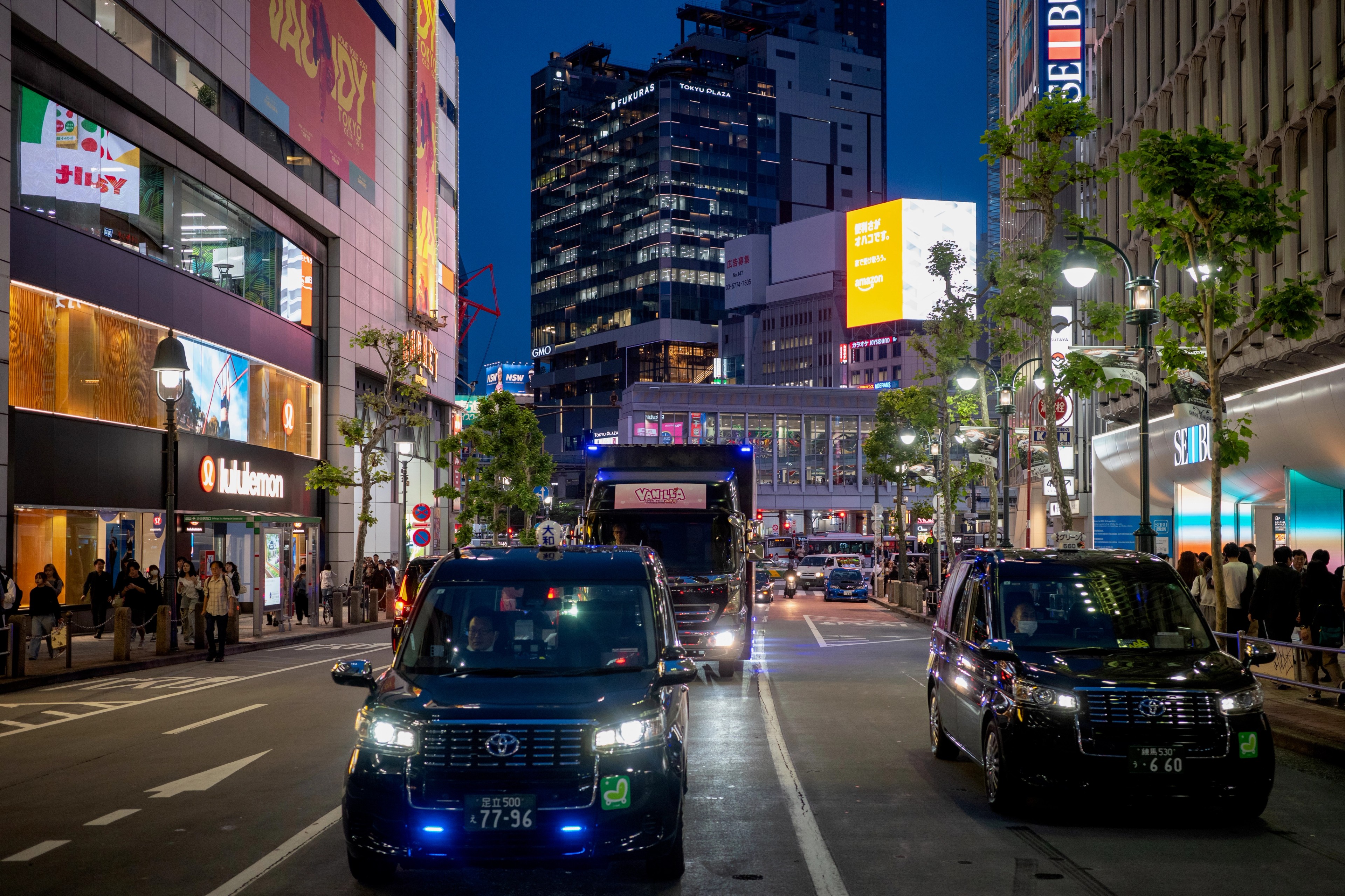 Taxis and storefronts line a busy city avenue at night.