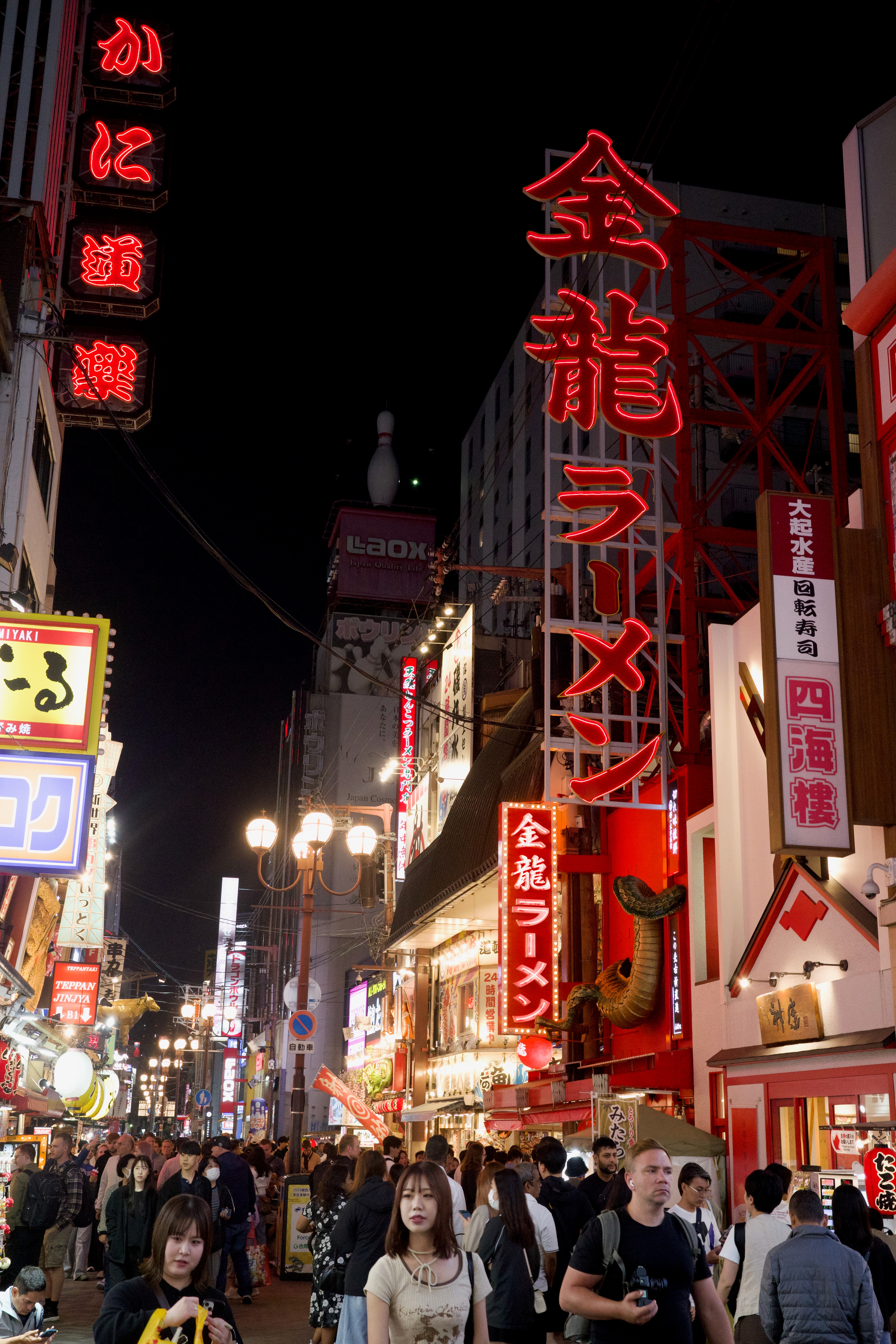 Crowds walk below tall red and white neon signs.