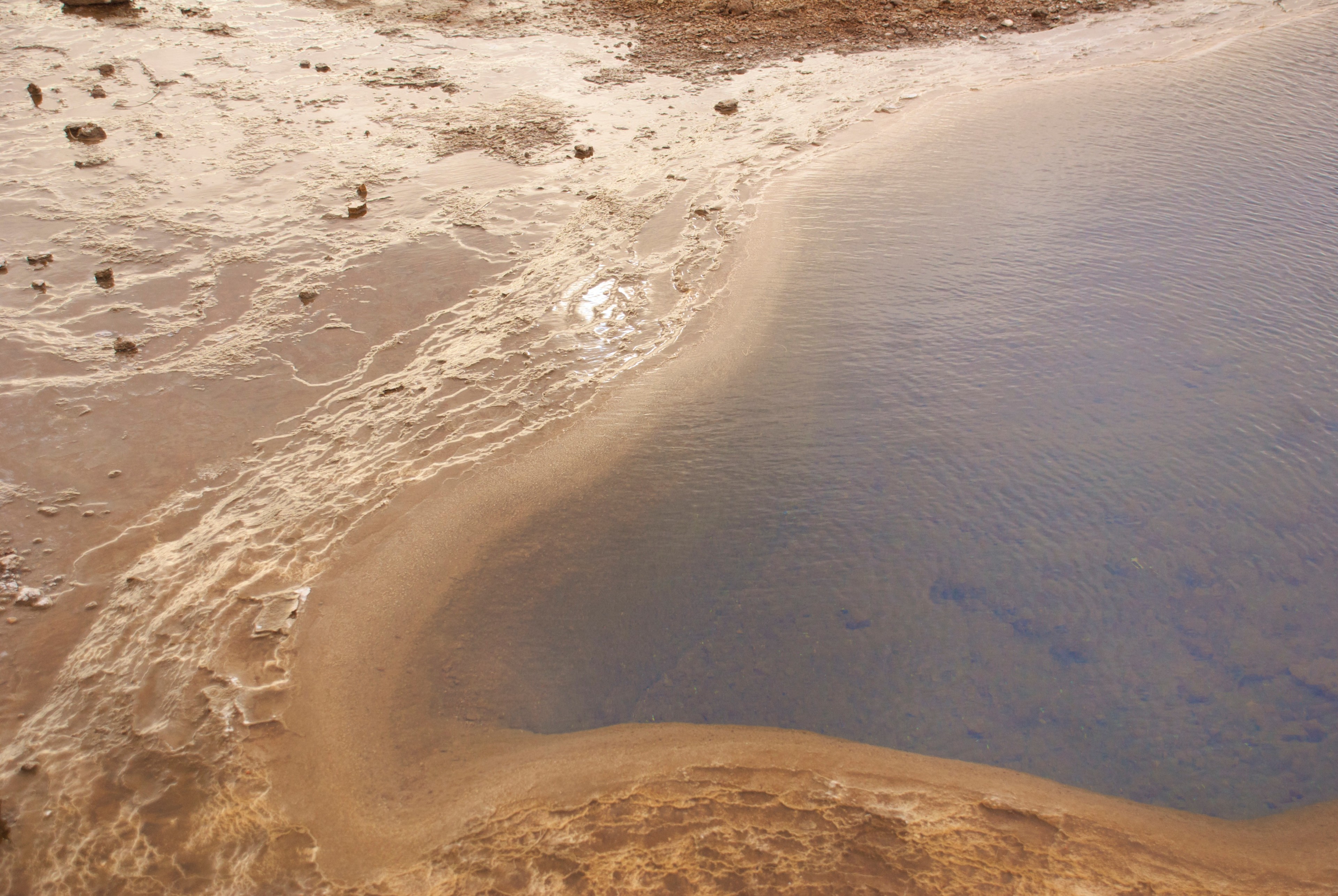 Aerial view of brown volcanic ground beside a pale stream or meltwater pool.