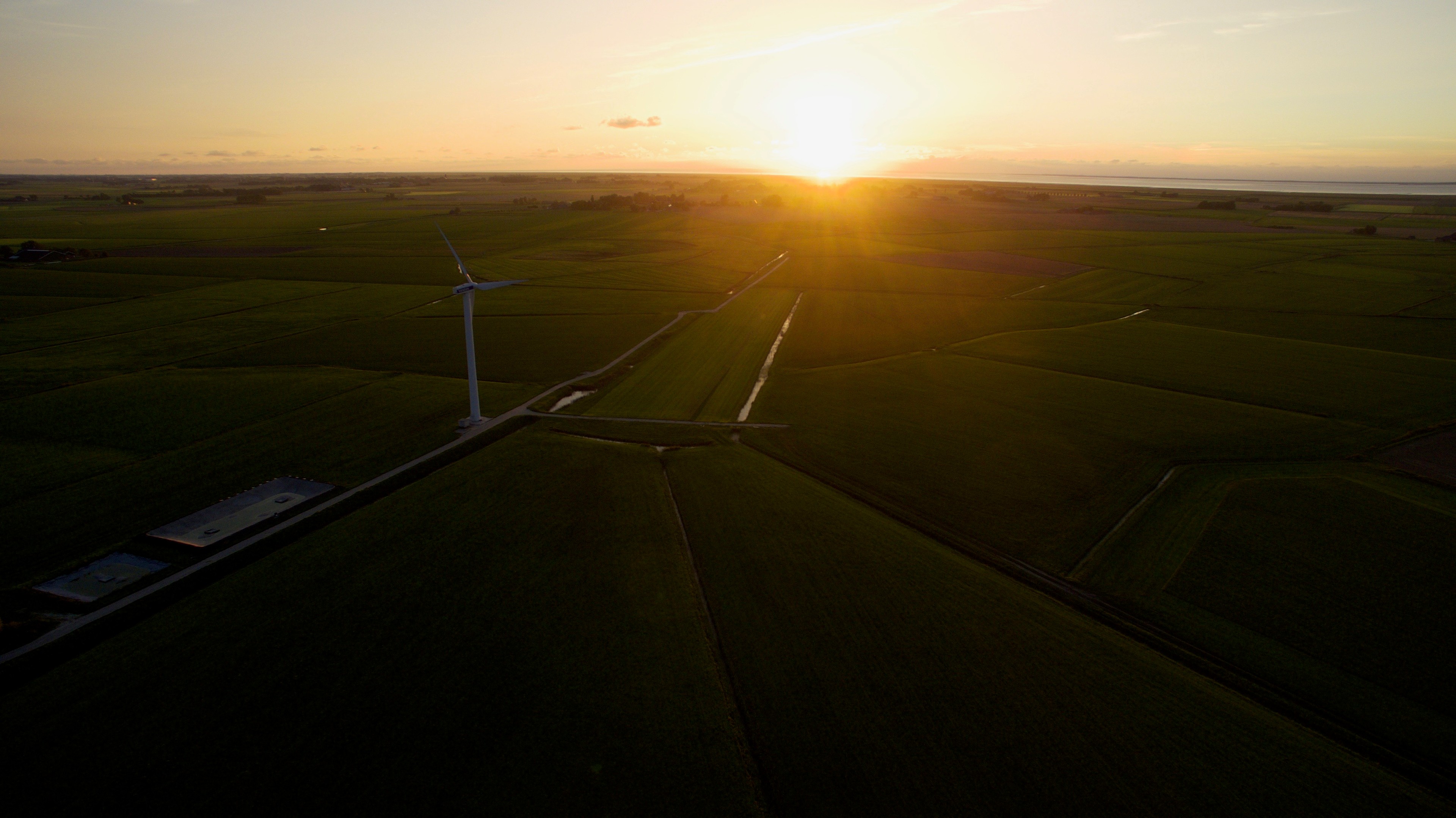 Sunset falls over flat fields and a wind turbine.