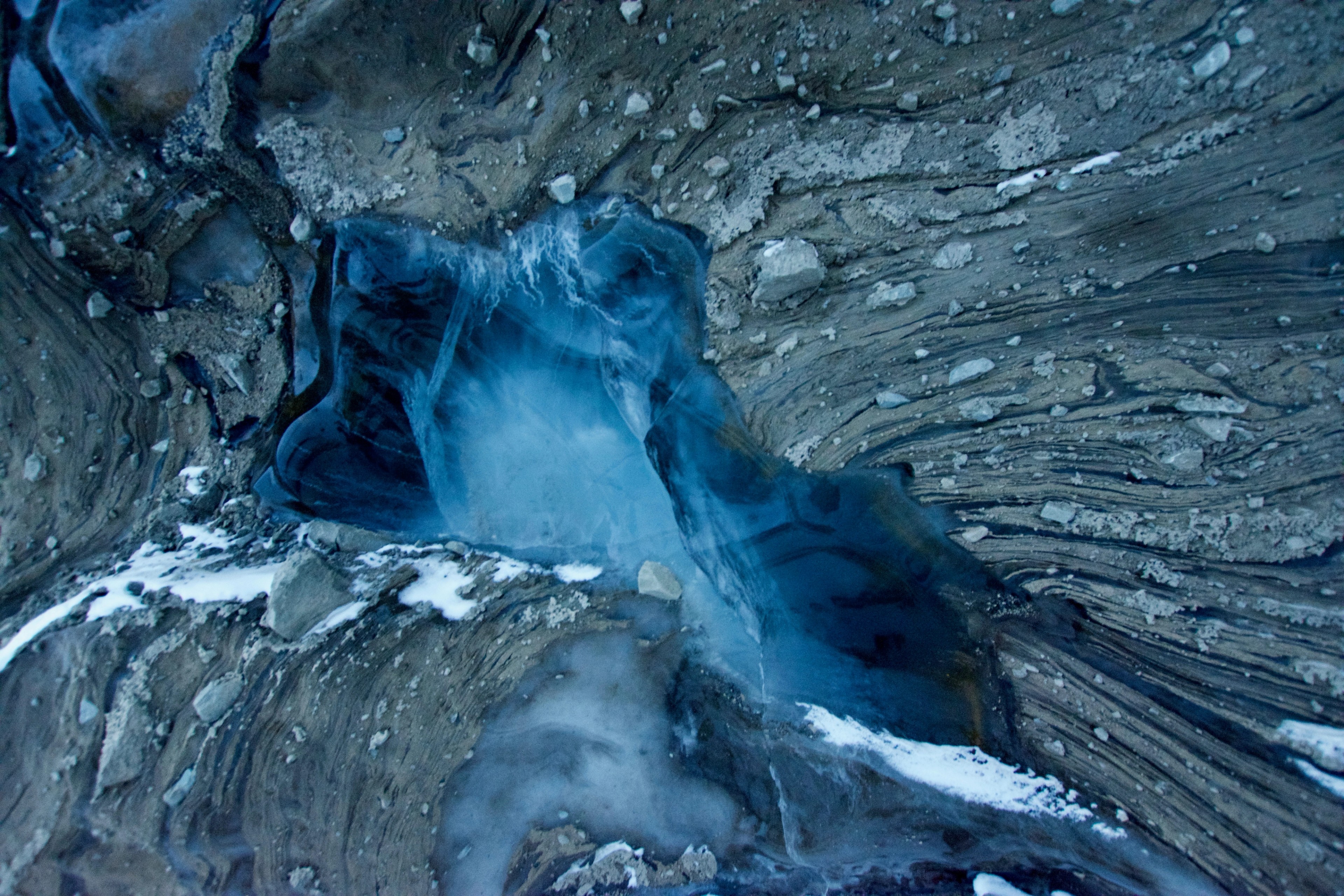 Blue meltwater flows through a crevasse in glacial ice.