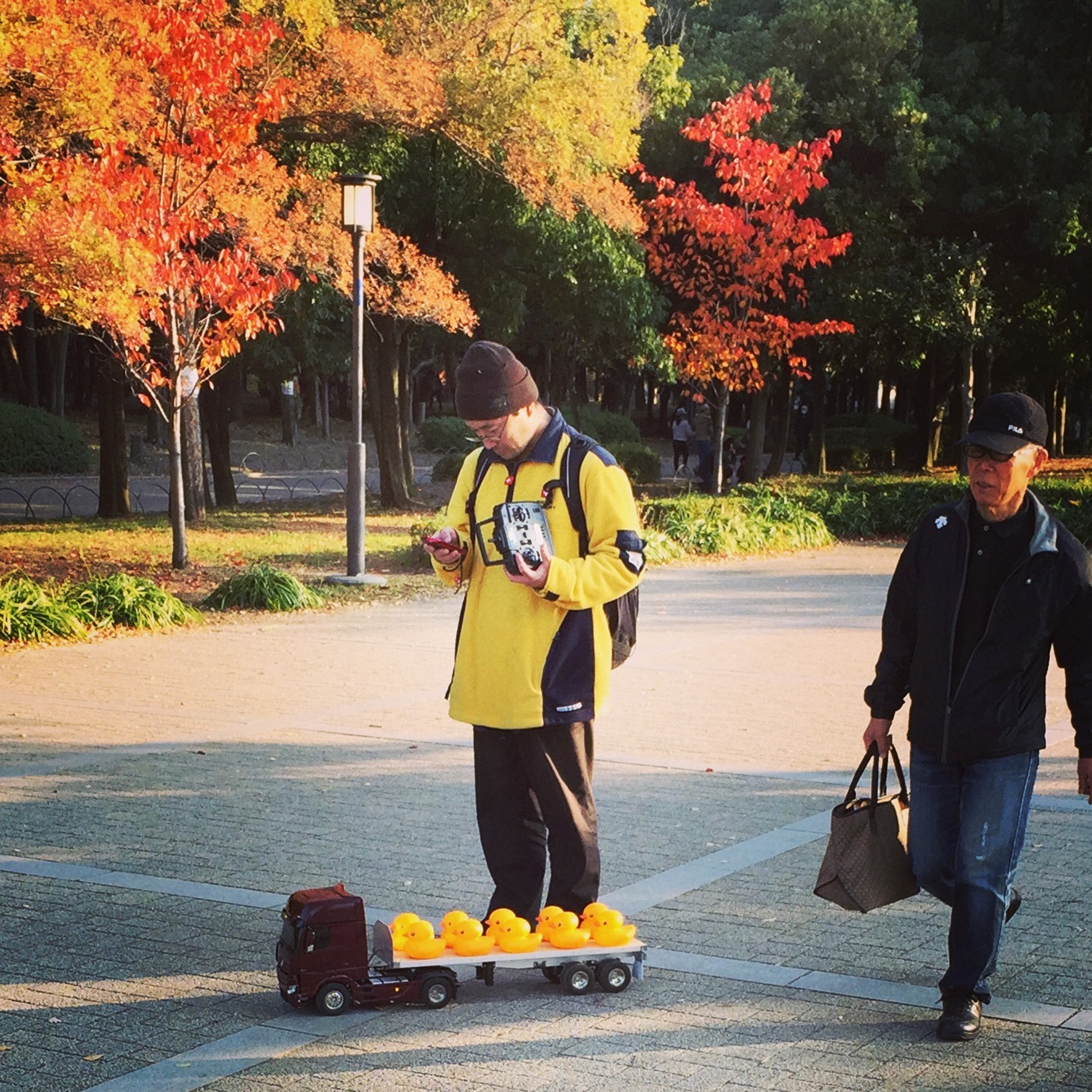 Two people stand on a path beneath bright autumn-colored trees.