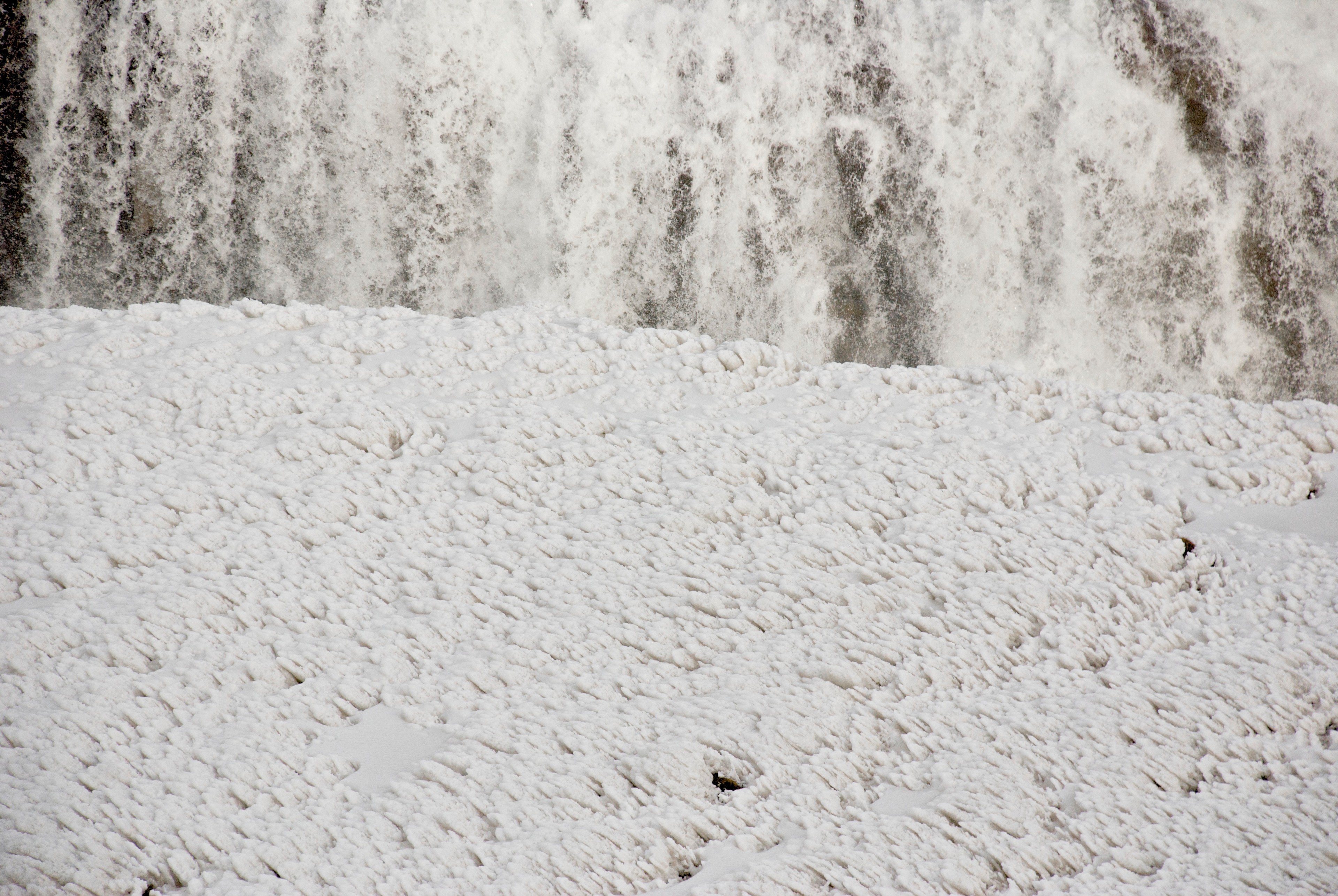 Water pours over a low cliff beside a thick bank of ice.