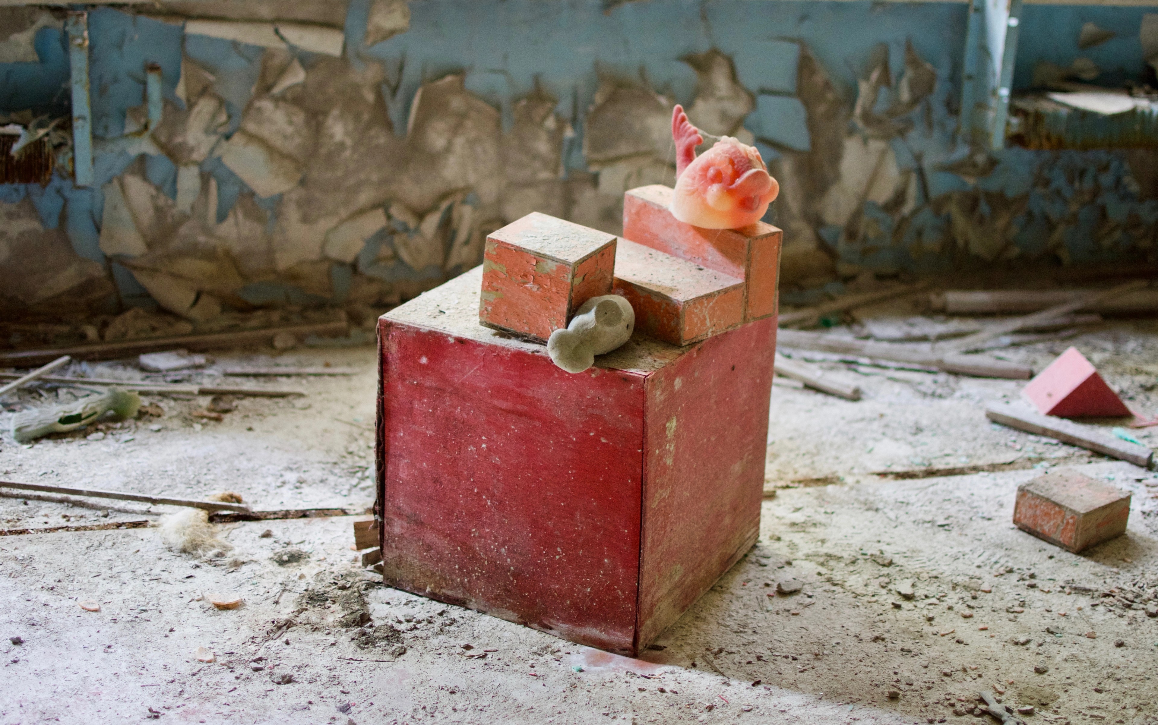Small toys sit on a red plinth in a ruined room.