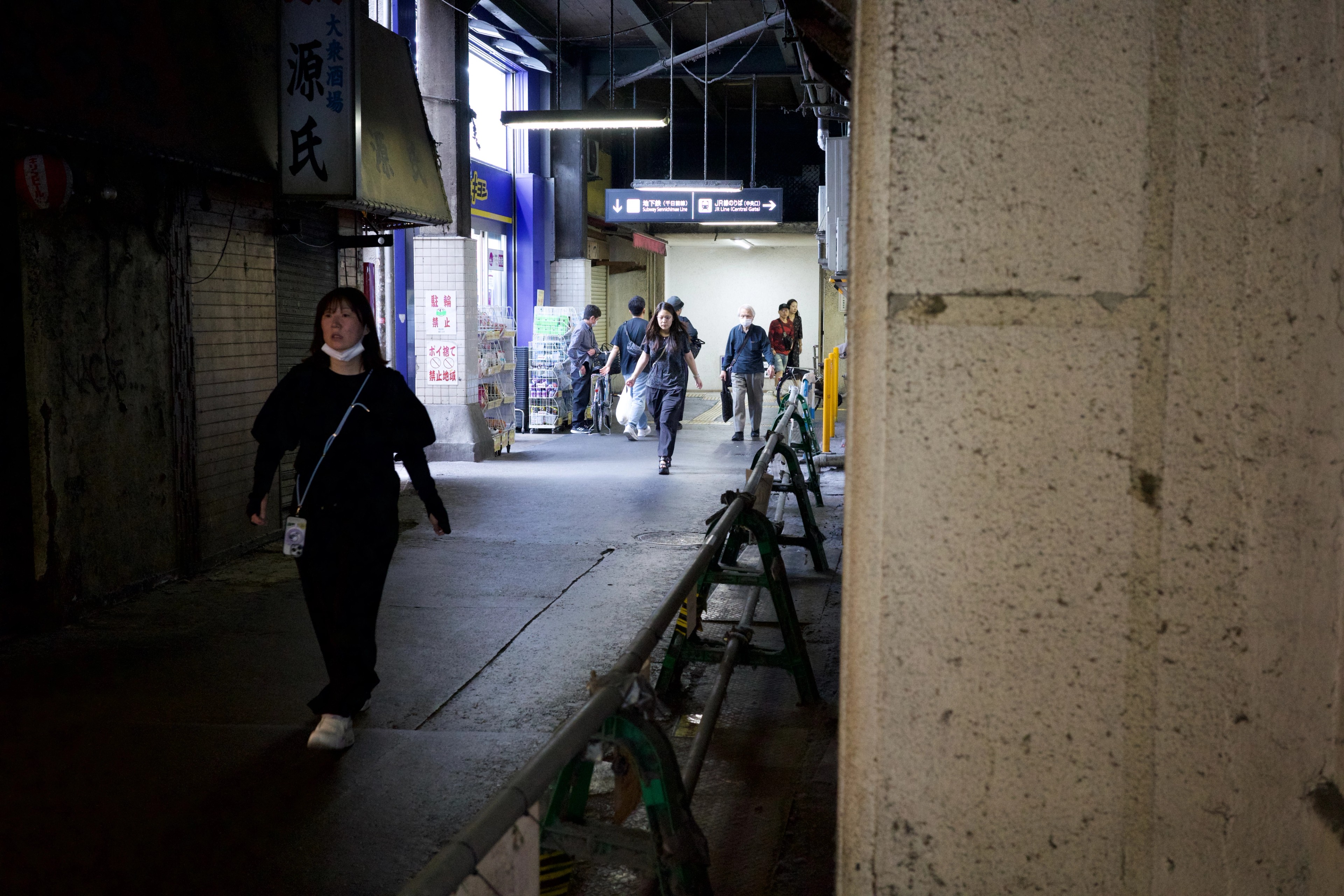 A person walks through a narrow alley beside a concrete wall.