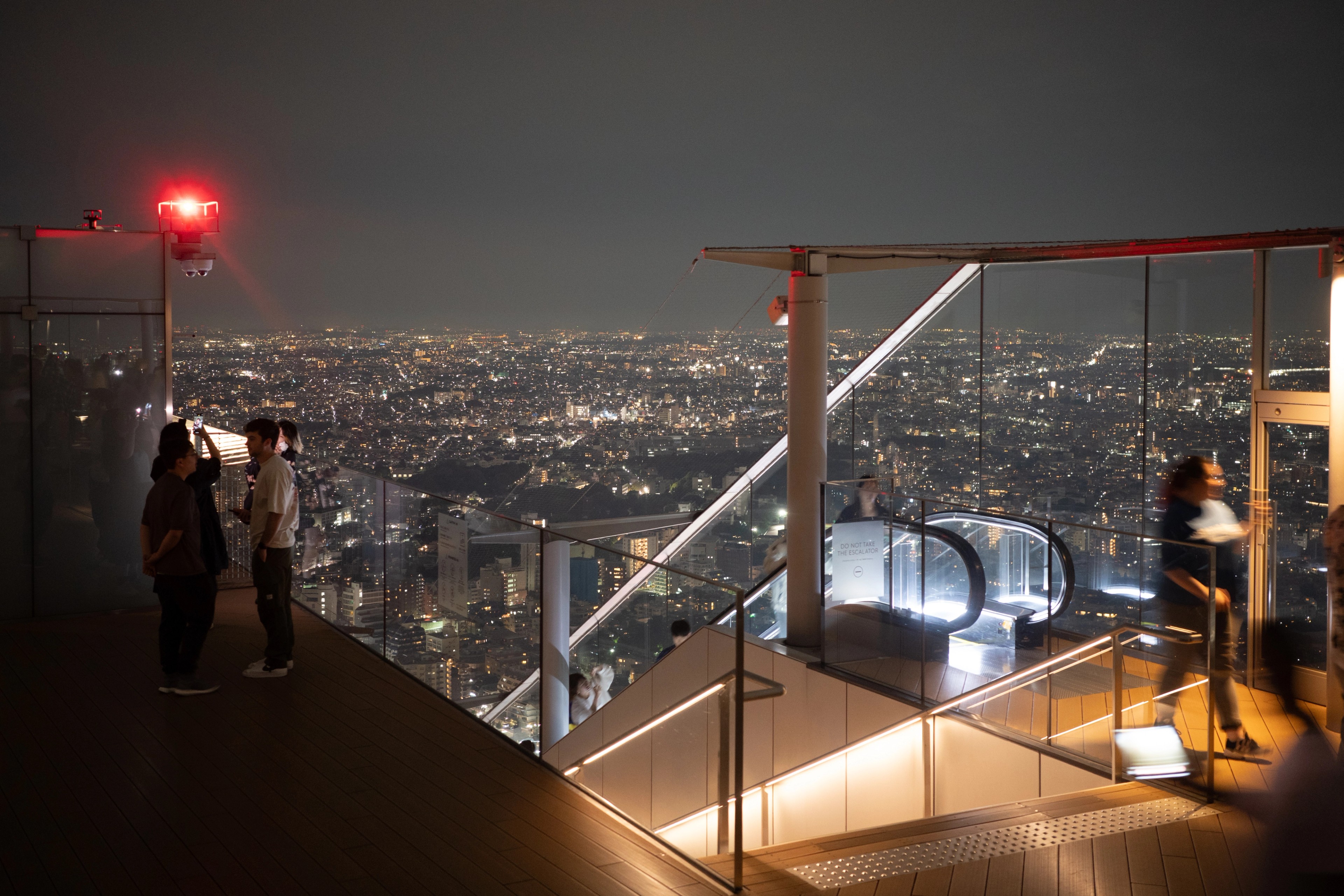 Two people look out over a city from an illuminated observation deck.