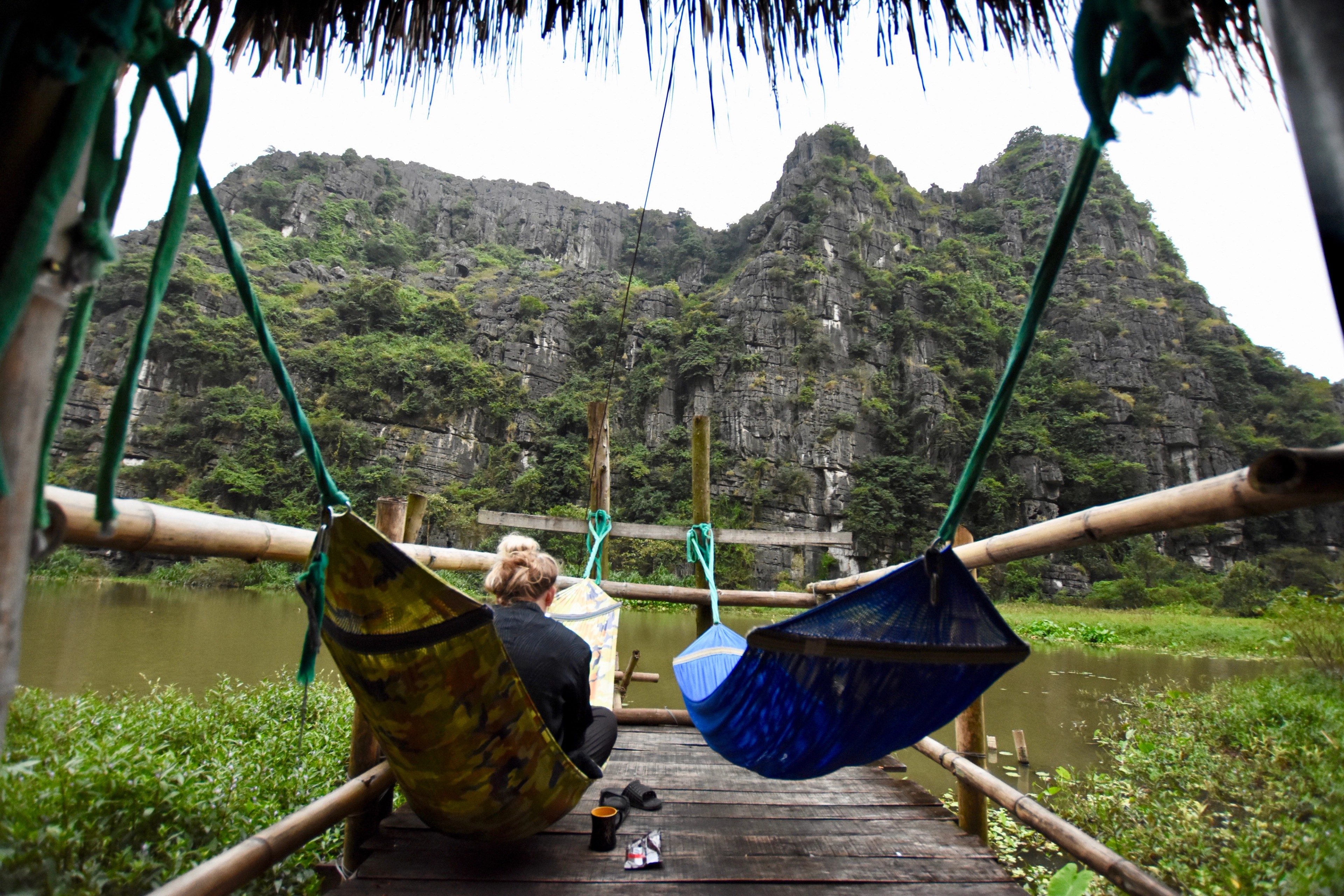 Two hammocks hang beneath a rustic shelter with limestone hills beyond.