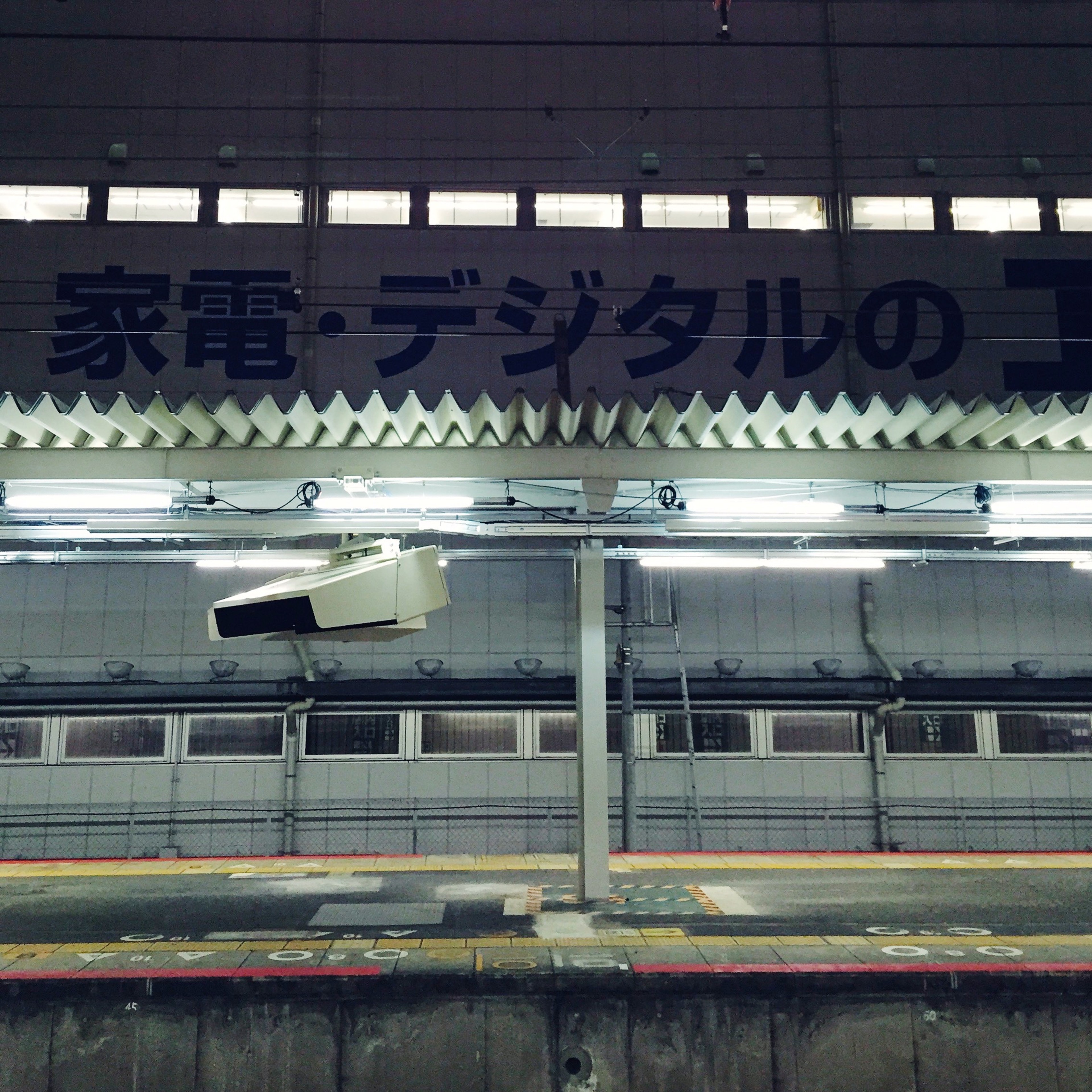 A train stands at a brightly lit station platform beneath a Japanese sign.