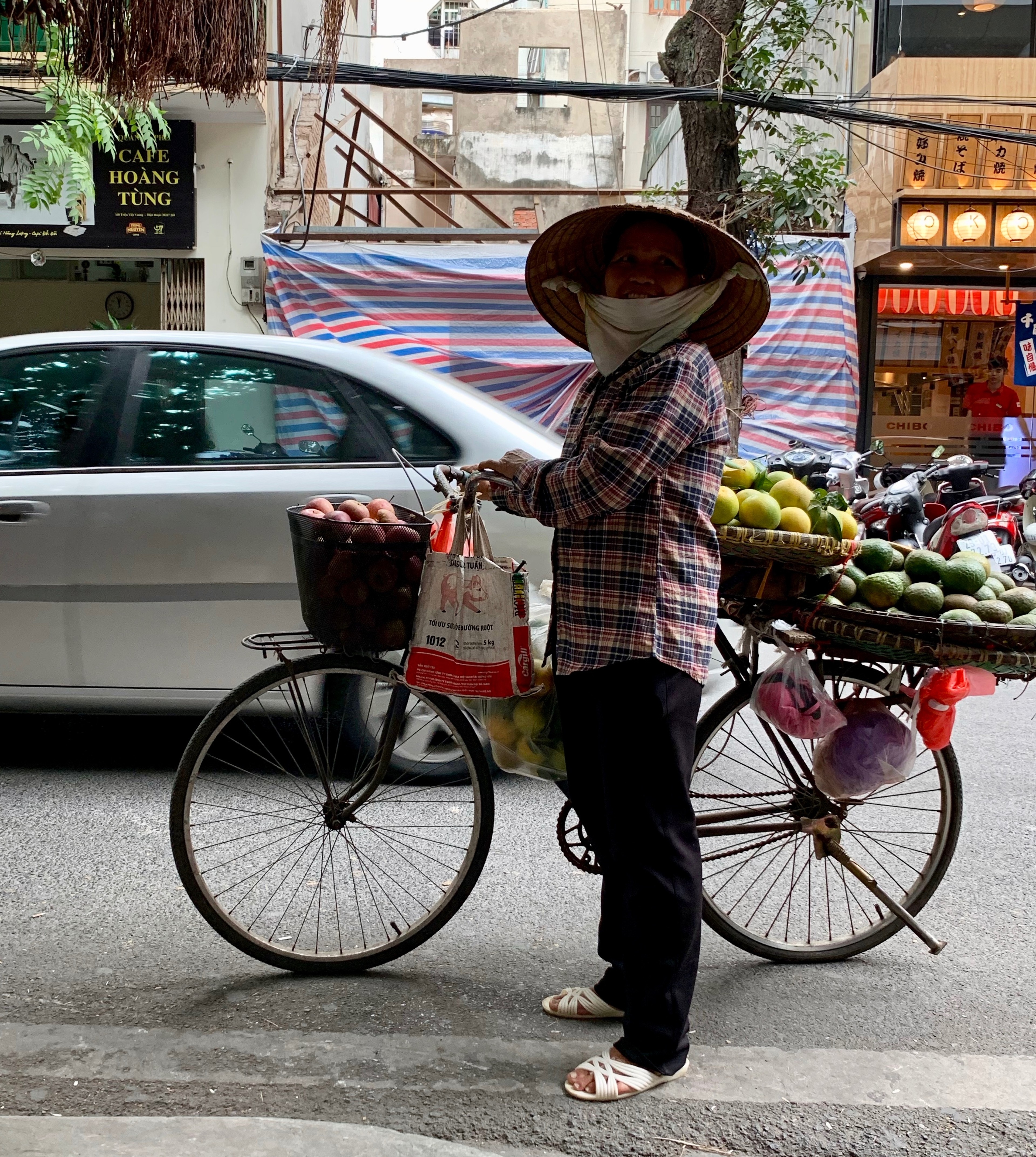 A vendor in a conical hat stands beside a bicycle carrying goods.