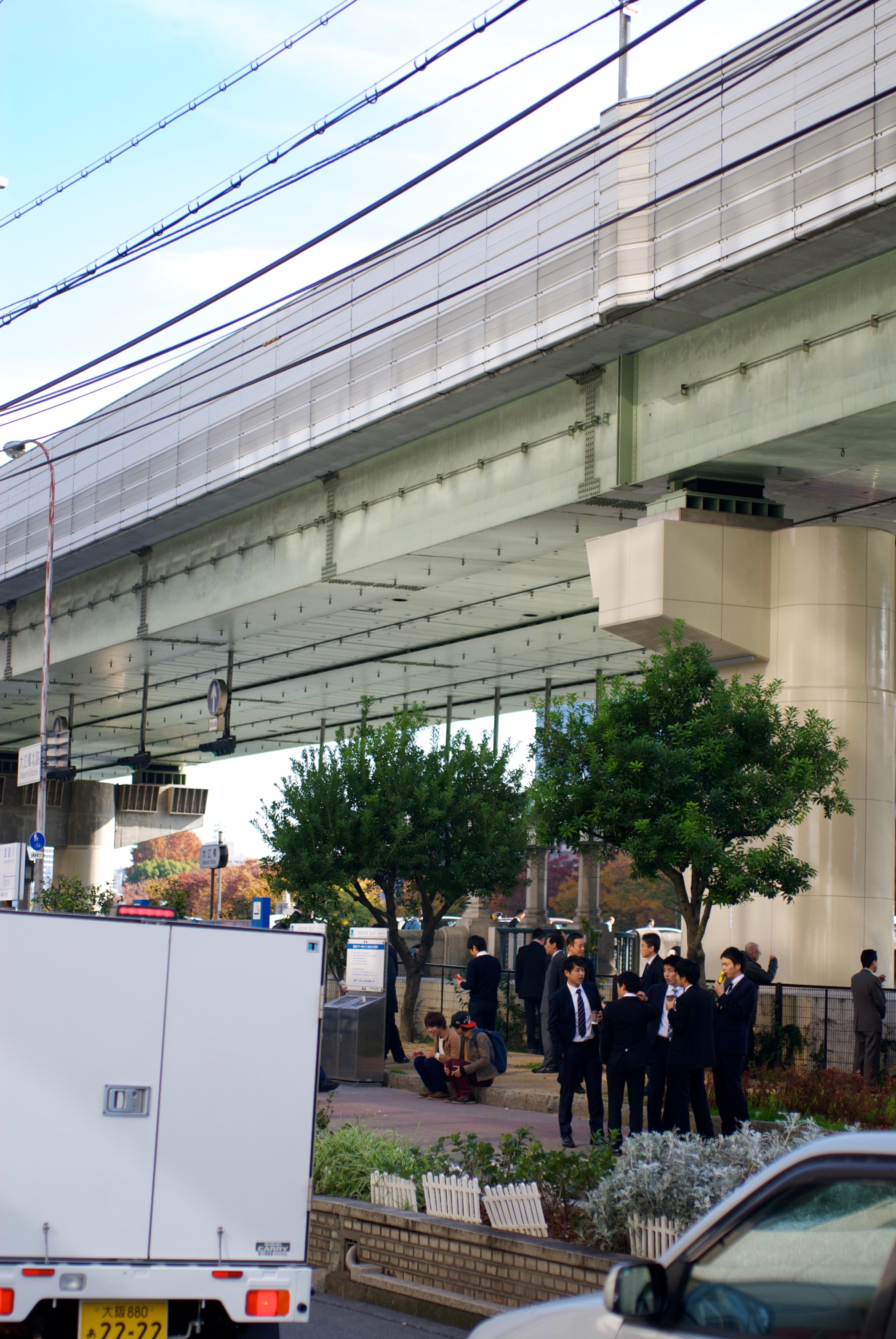 A busy sidewalk and street sit beneath an elevated road.