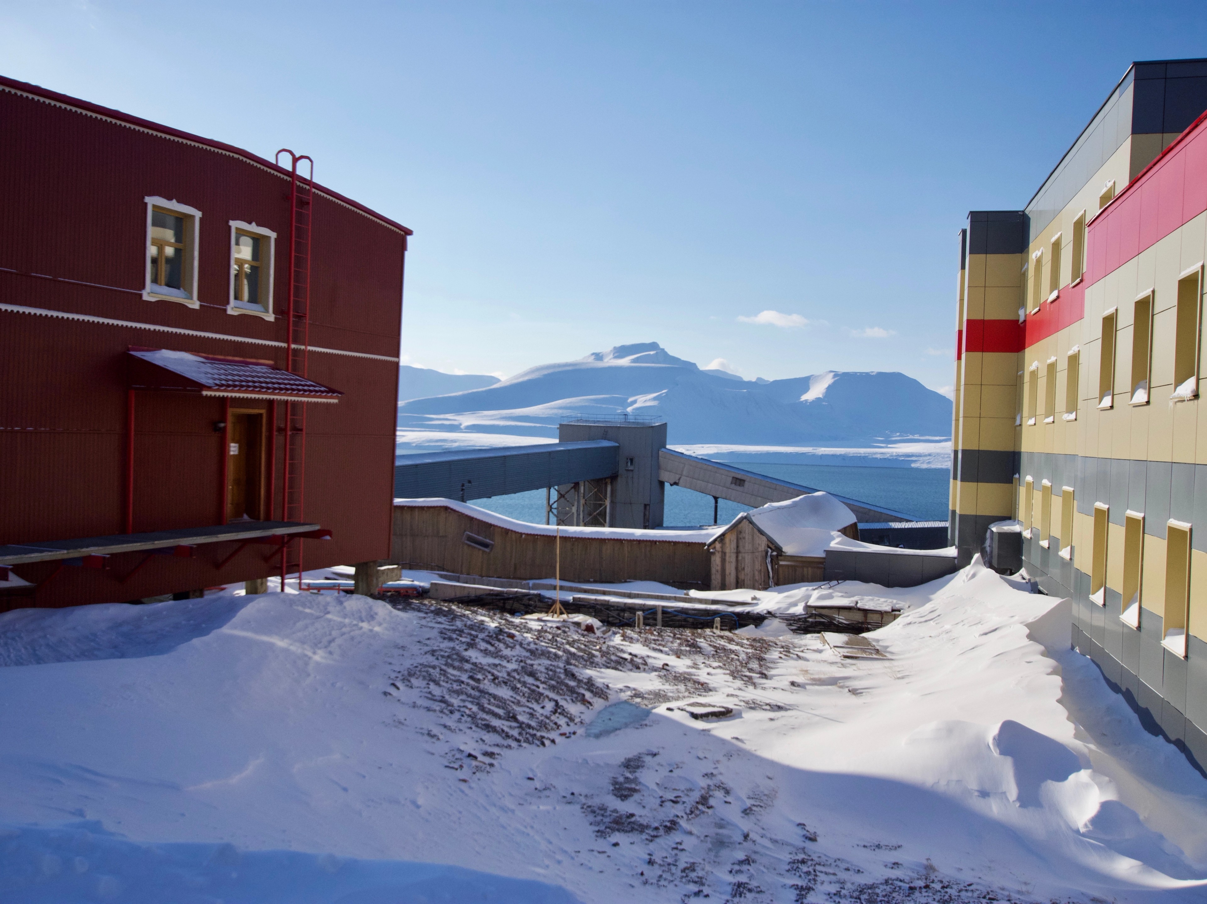A snowy lane between red and yellow buildings.