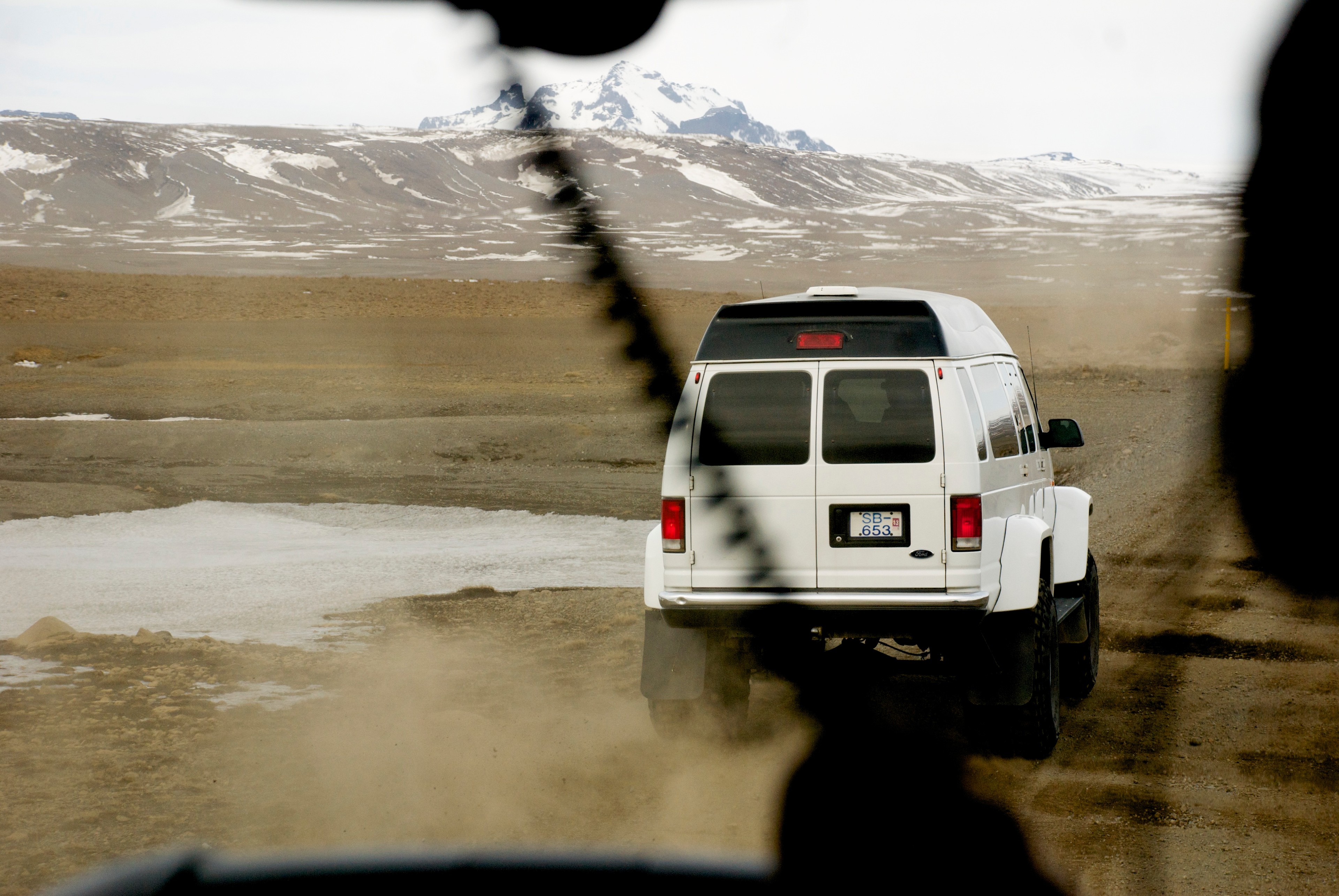 A white four-wheel-drive vehicle crosses a wet track, seen through the windshield.