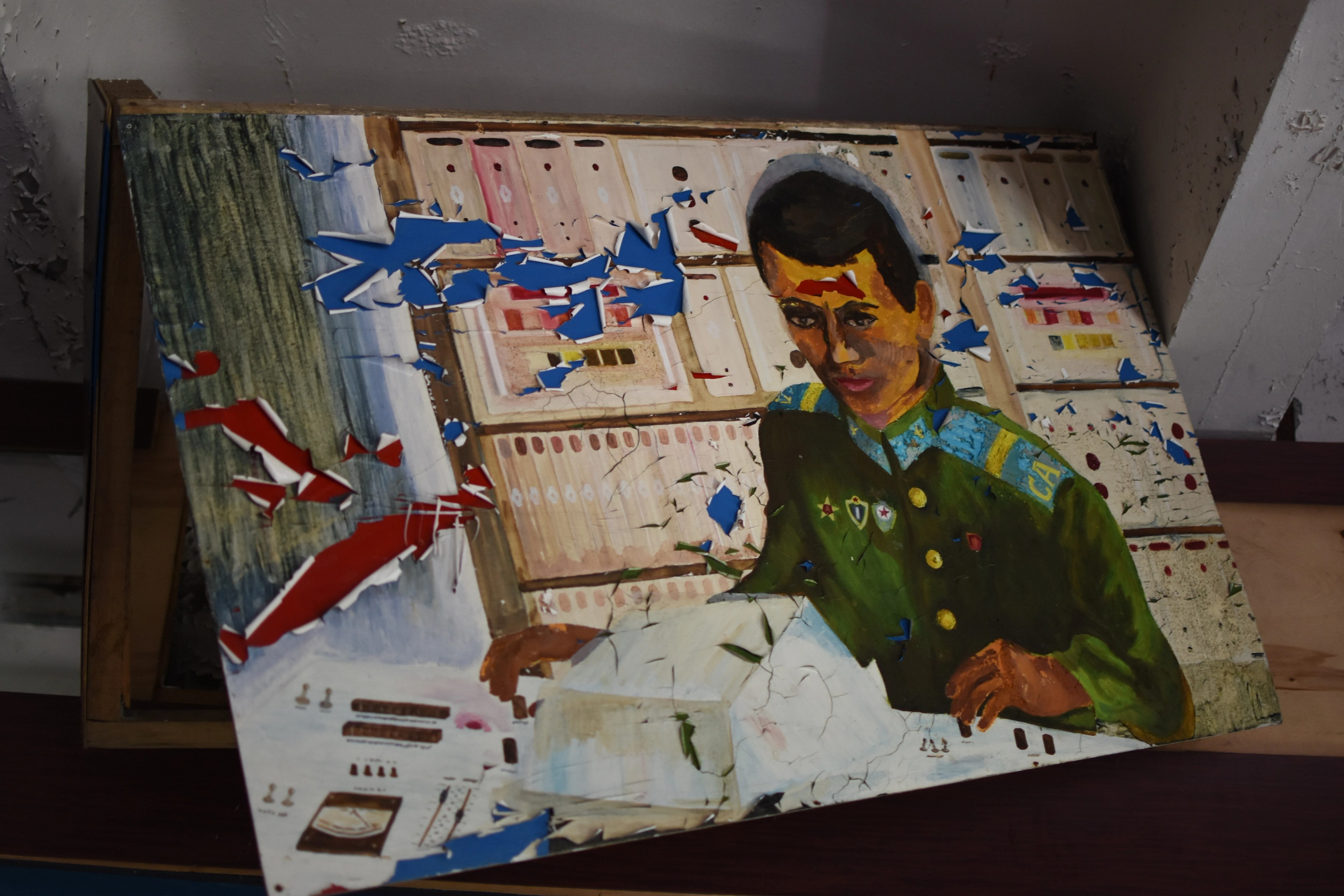 A torn poster depicting a uniformed man rests on a shelf.