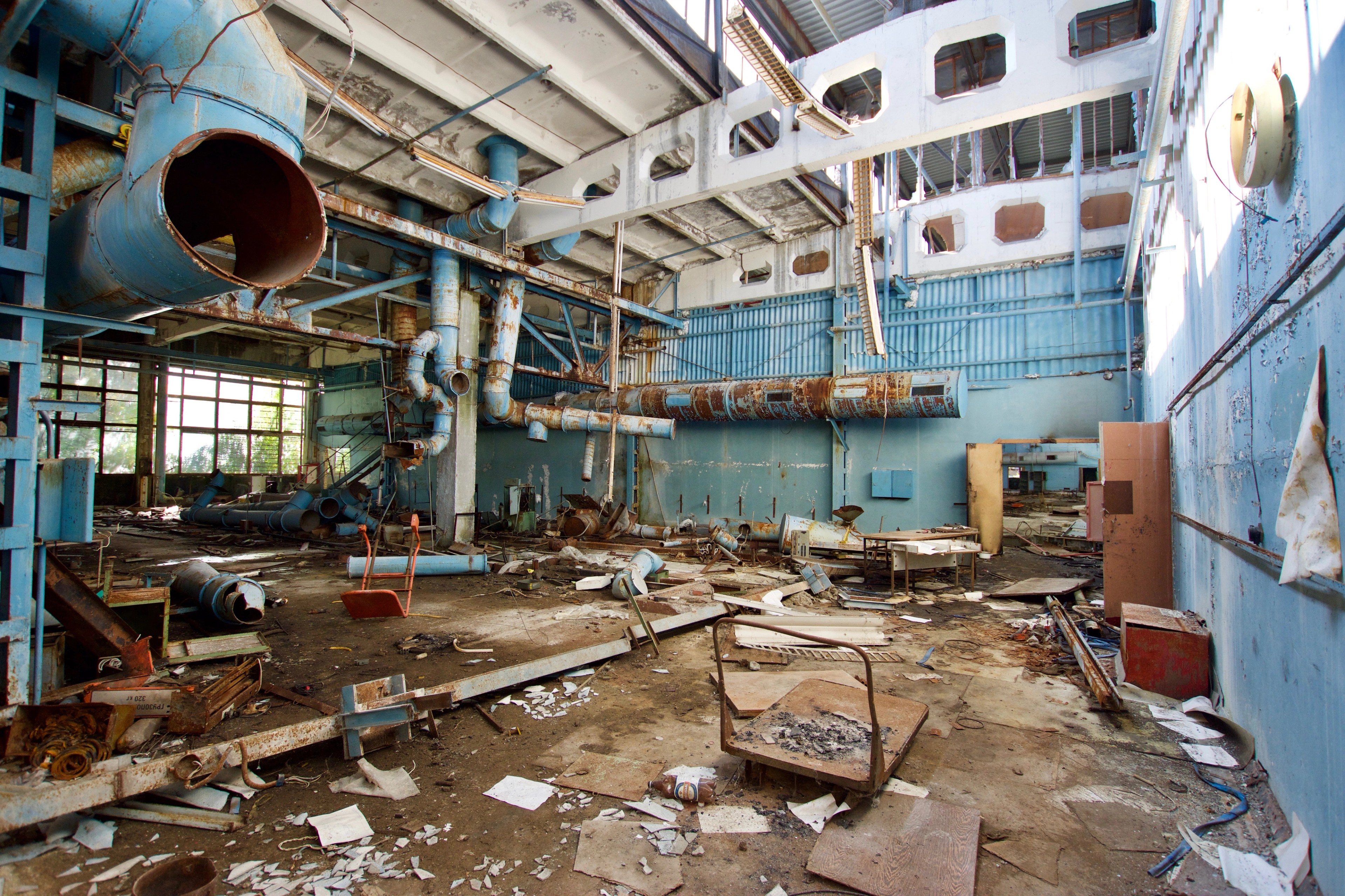 Blue machinery, pipes, and debris fill an industrial room.