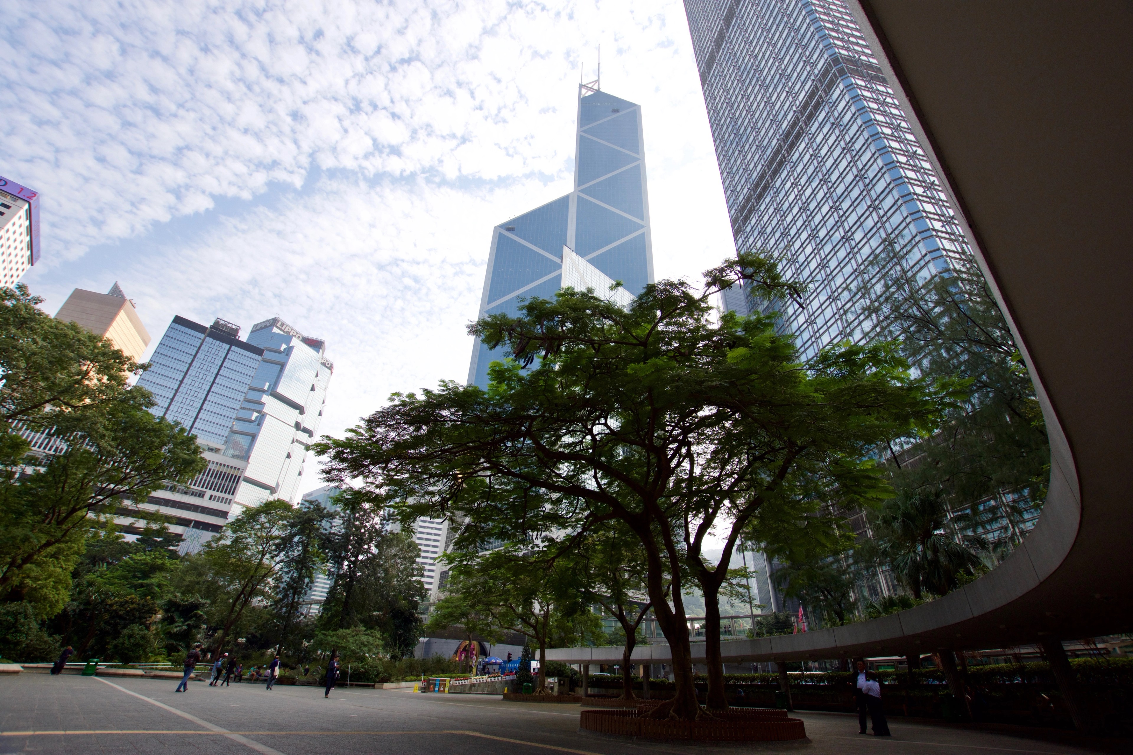 A curved white building stands among trees and glass towers.