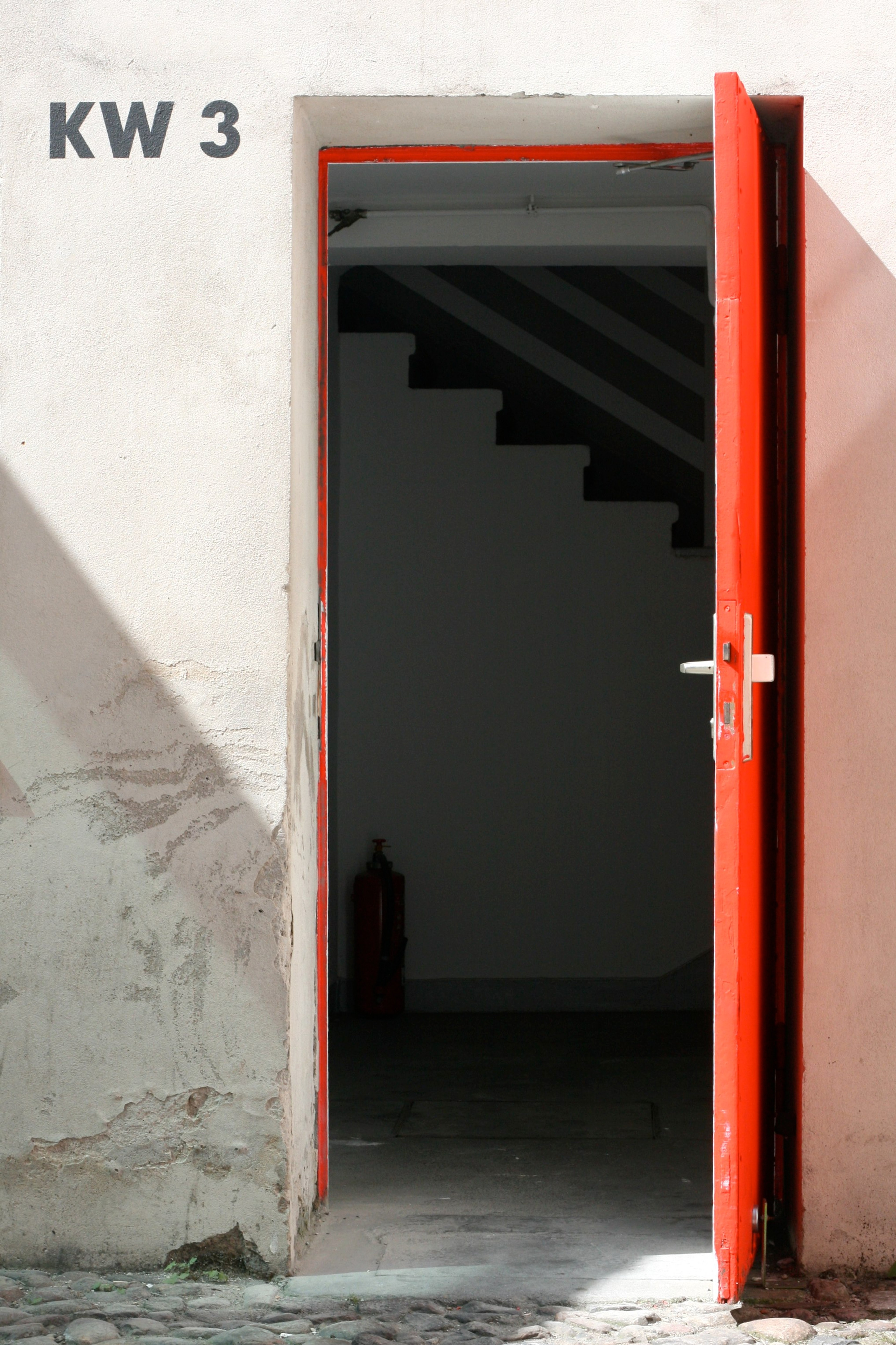A dark stairwell doorway with a red frame is set into a worn wall.
