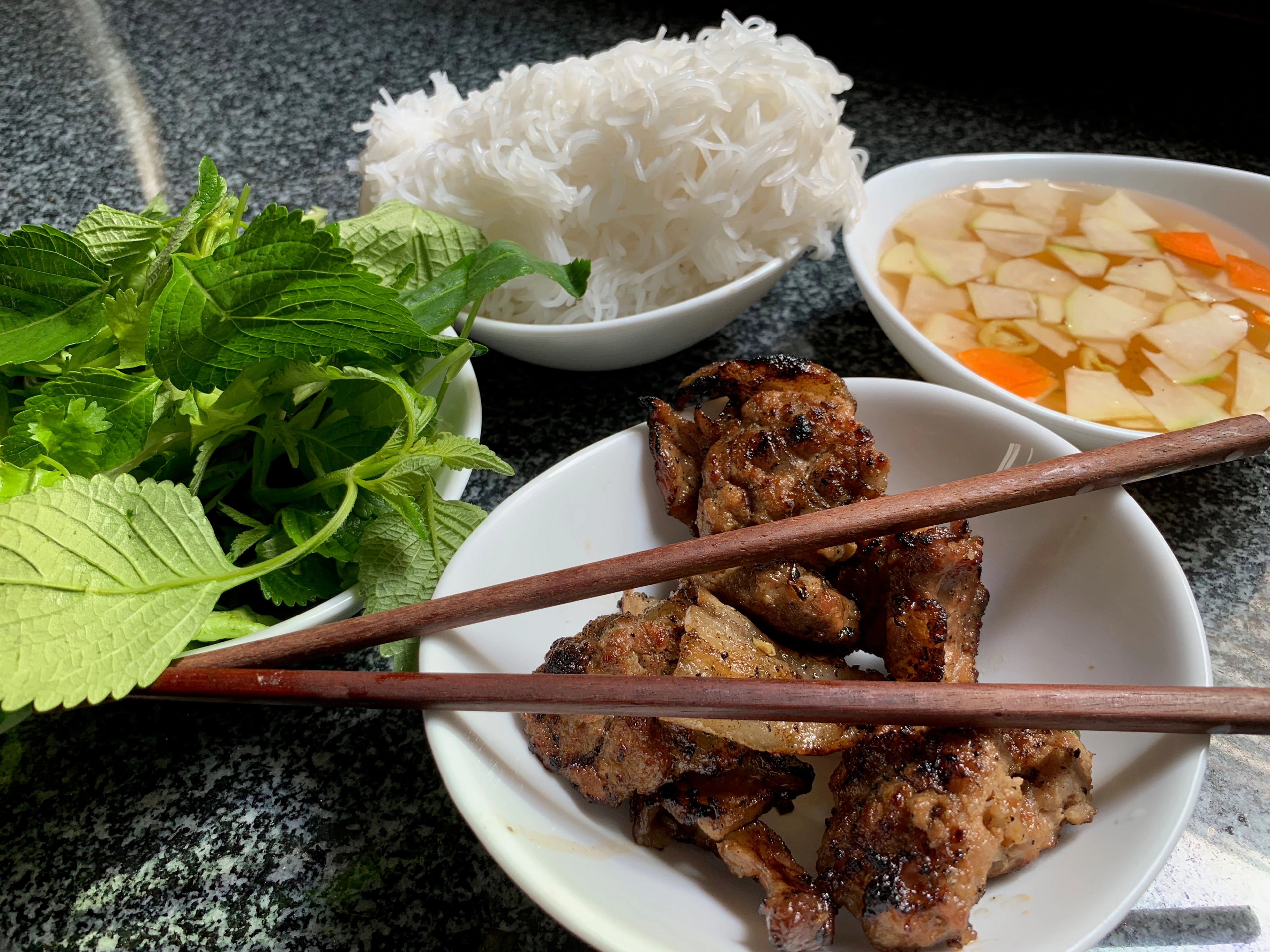 A plate of meat, herbs, rice, and dipping sauce is served with chopsticks.