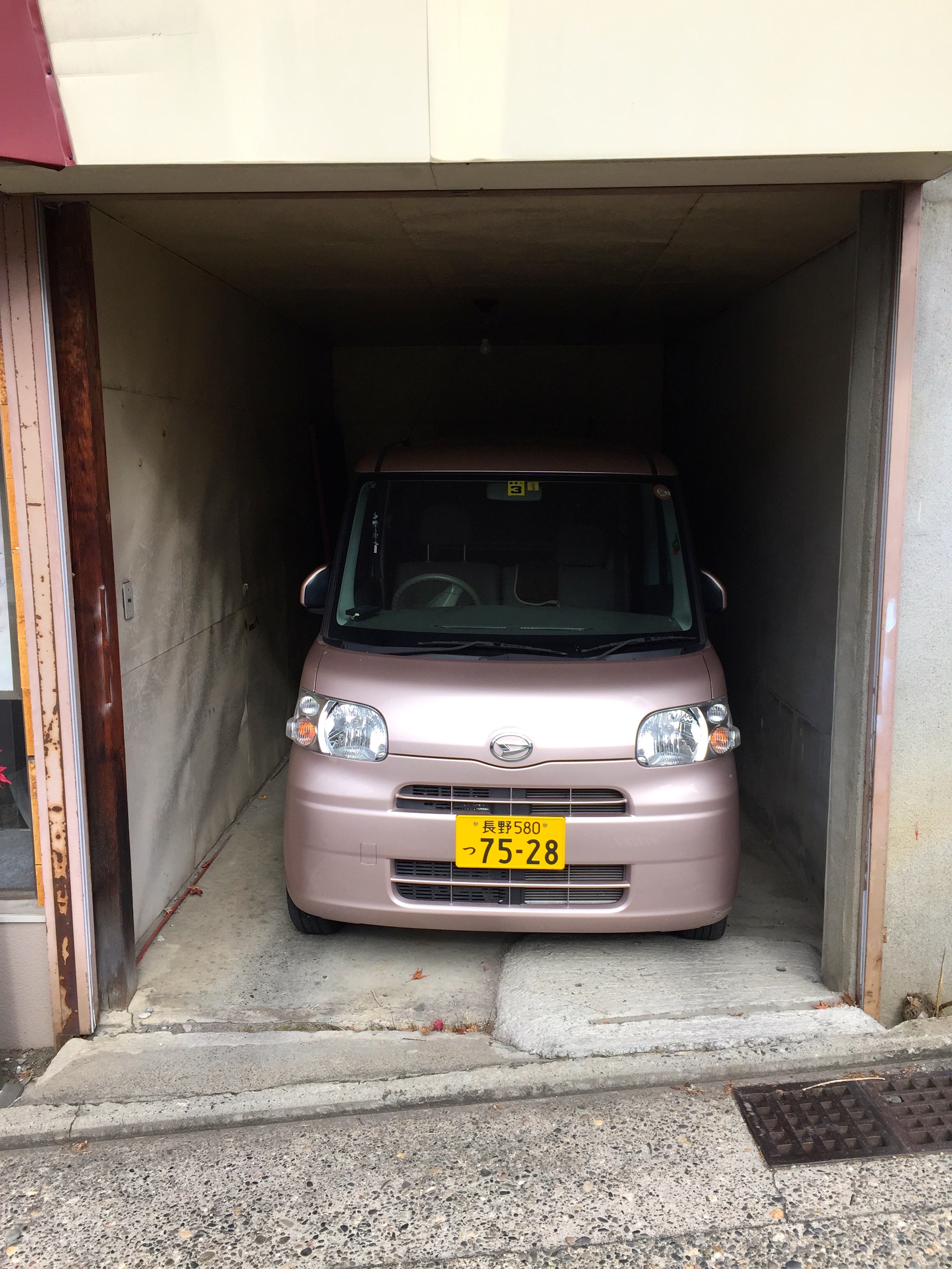 A small car is parked inside a narrow garage.
