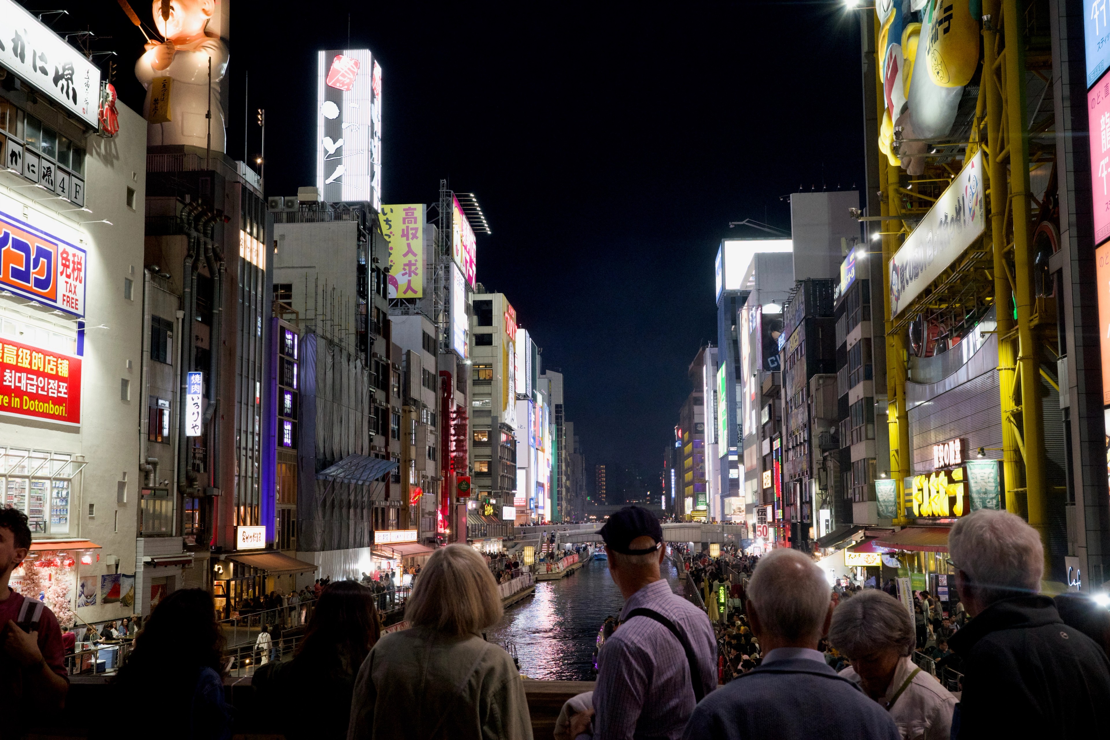 A crowd walks beneath neon signs on a busy night street.