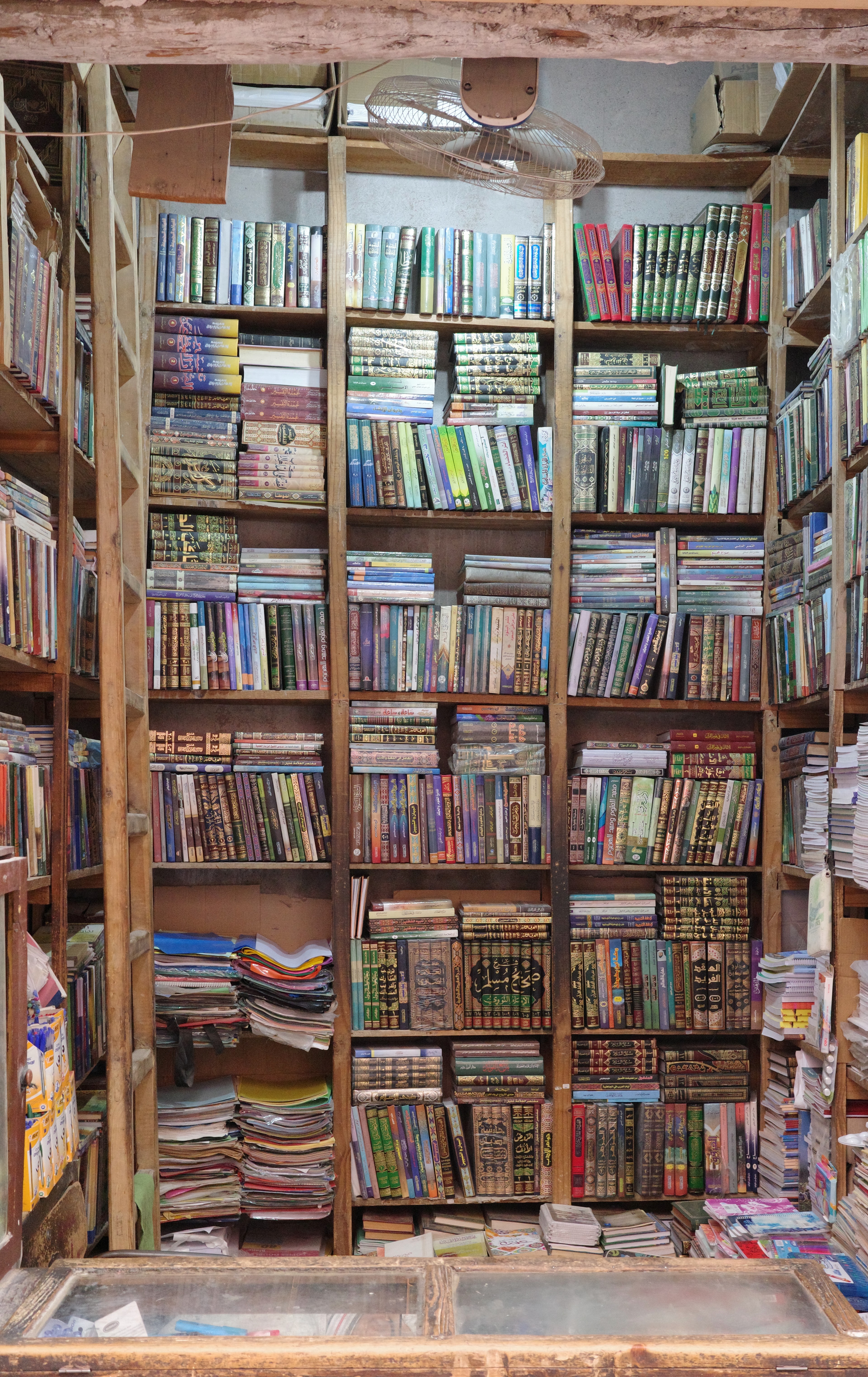 A narrow bookshop is packed with rows of books and printed materials.