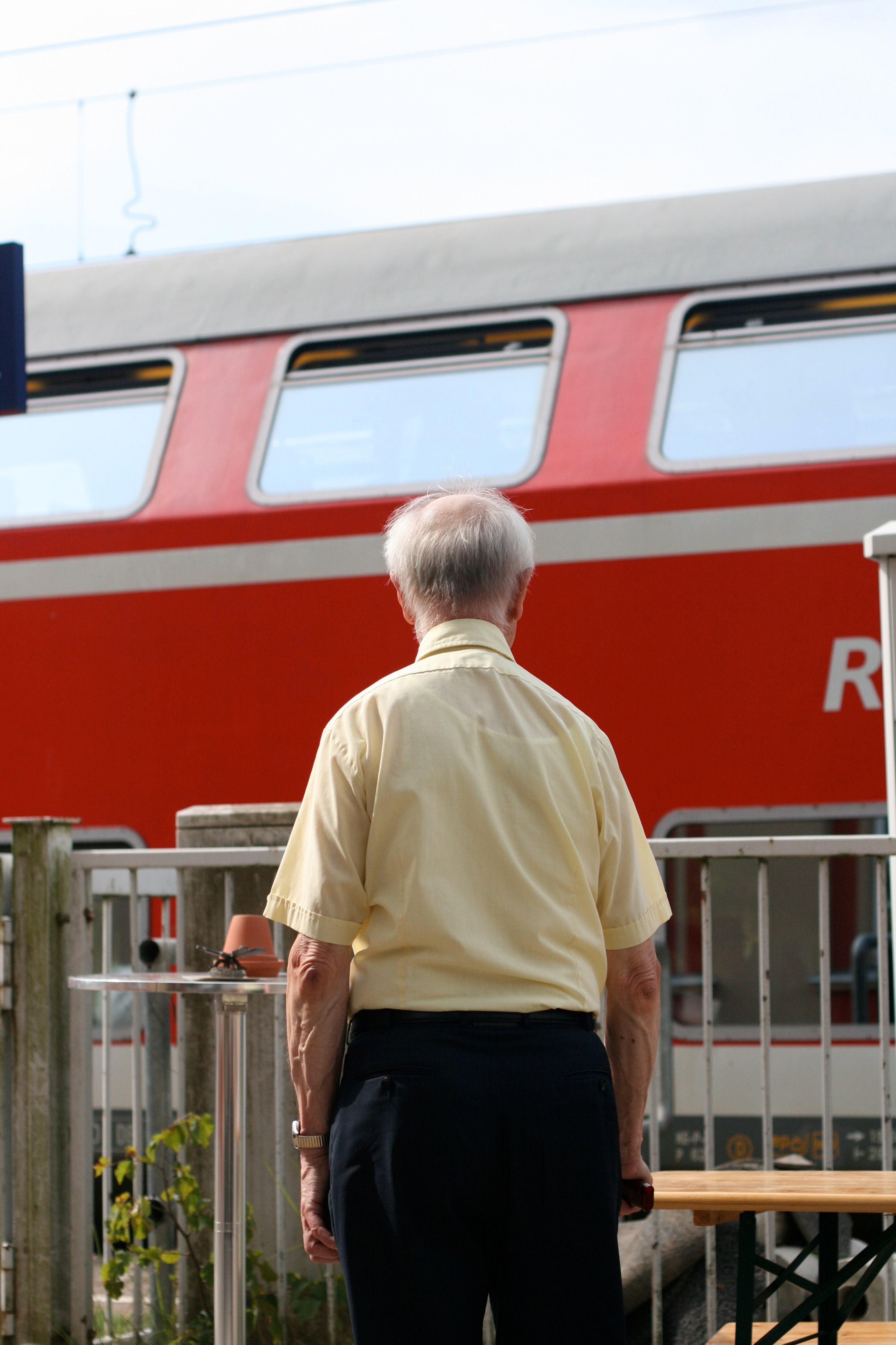 An older man stands on a station platform beside a red-and-white train.