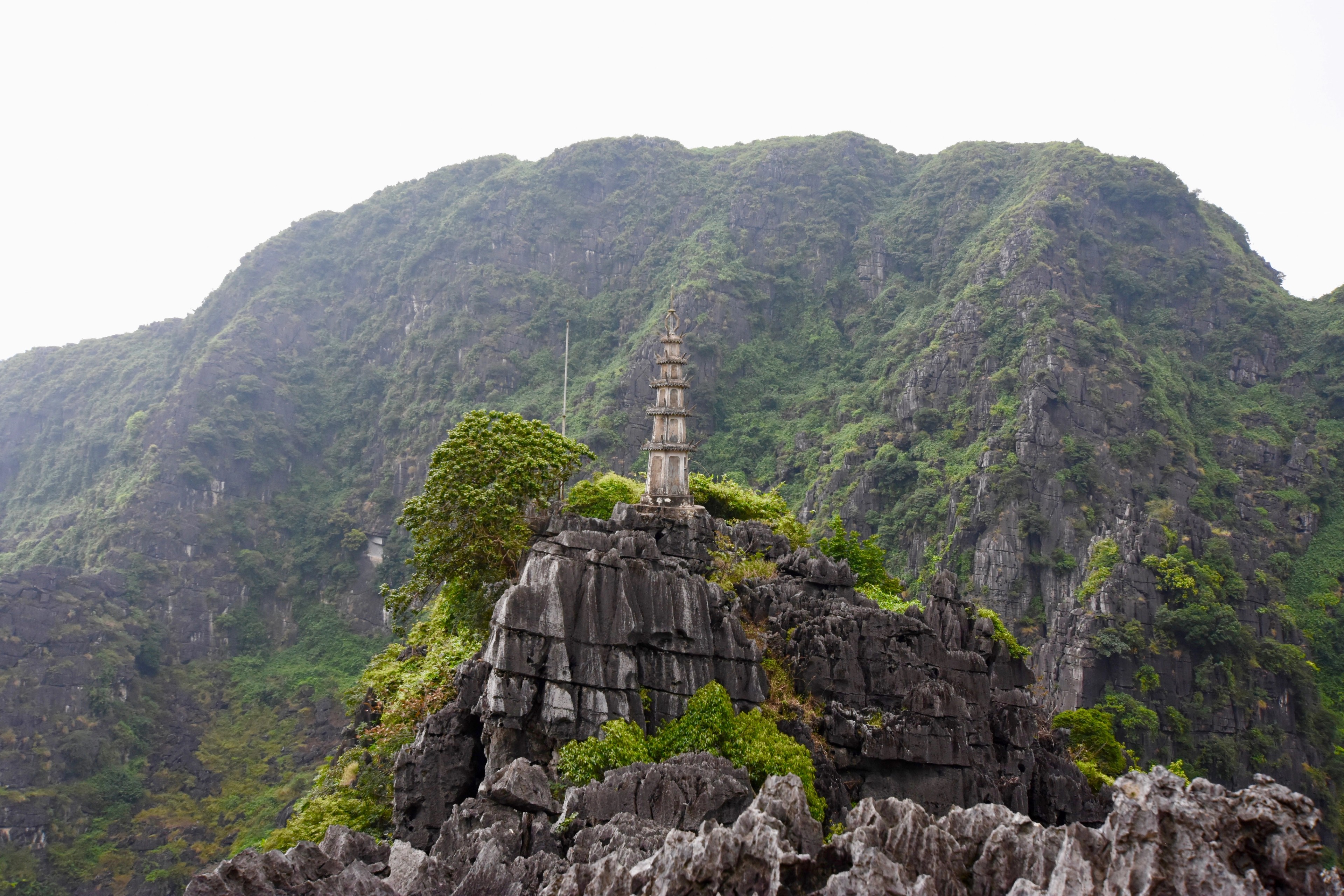 A small stone pagoda stands on a rocky ridge above a green valley.