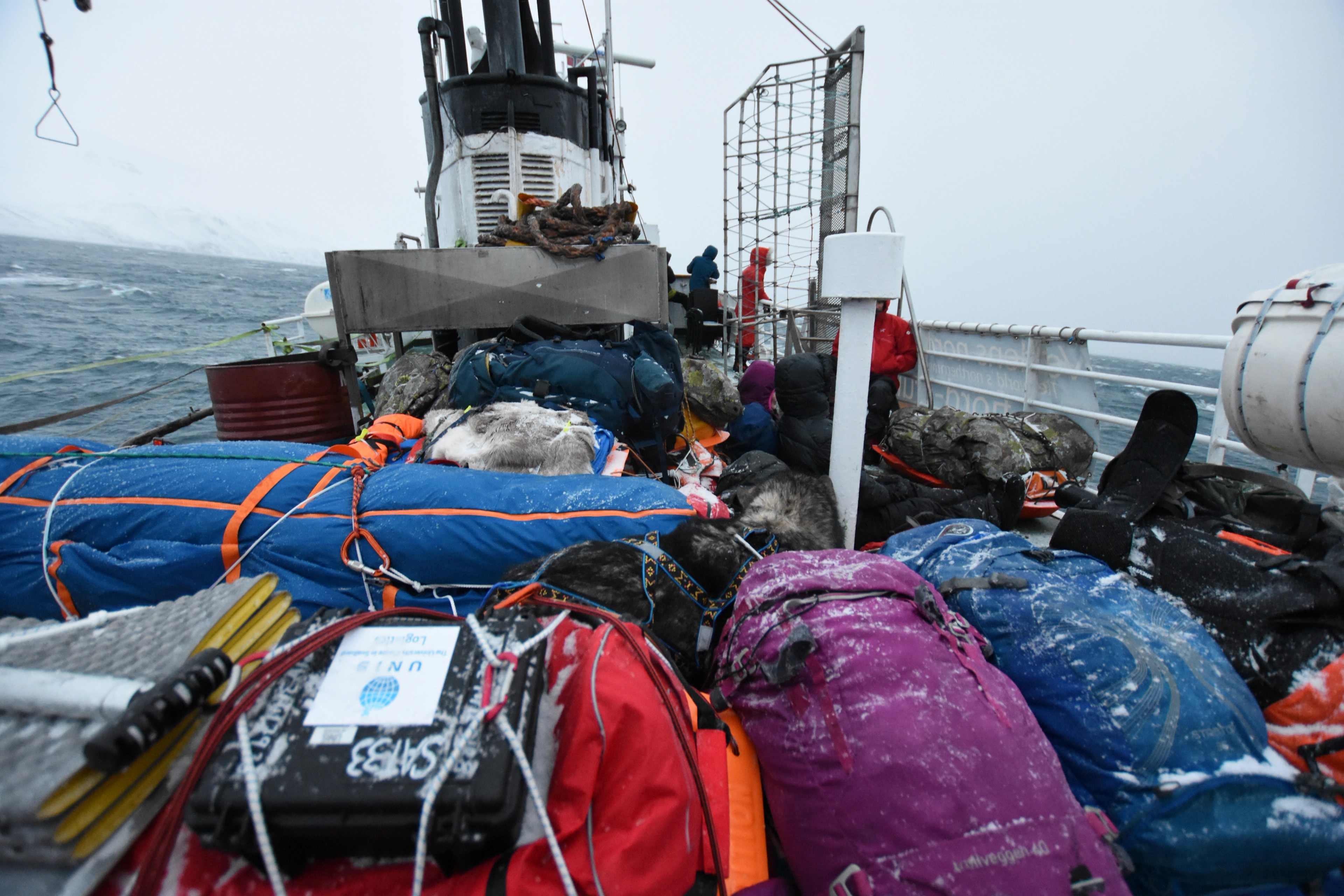 Cargo and colorful bags are secured on a boat deck.
